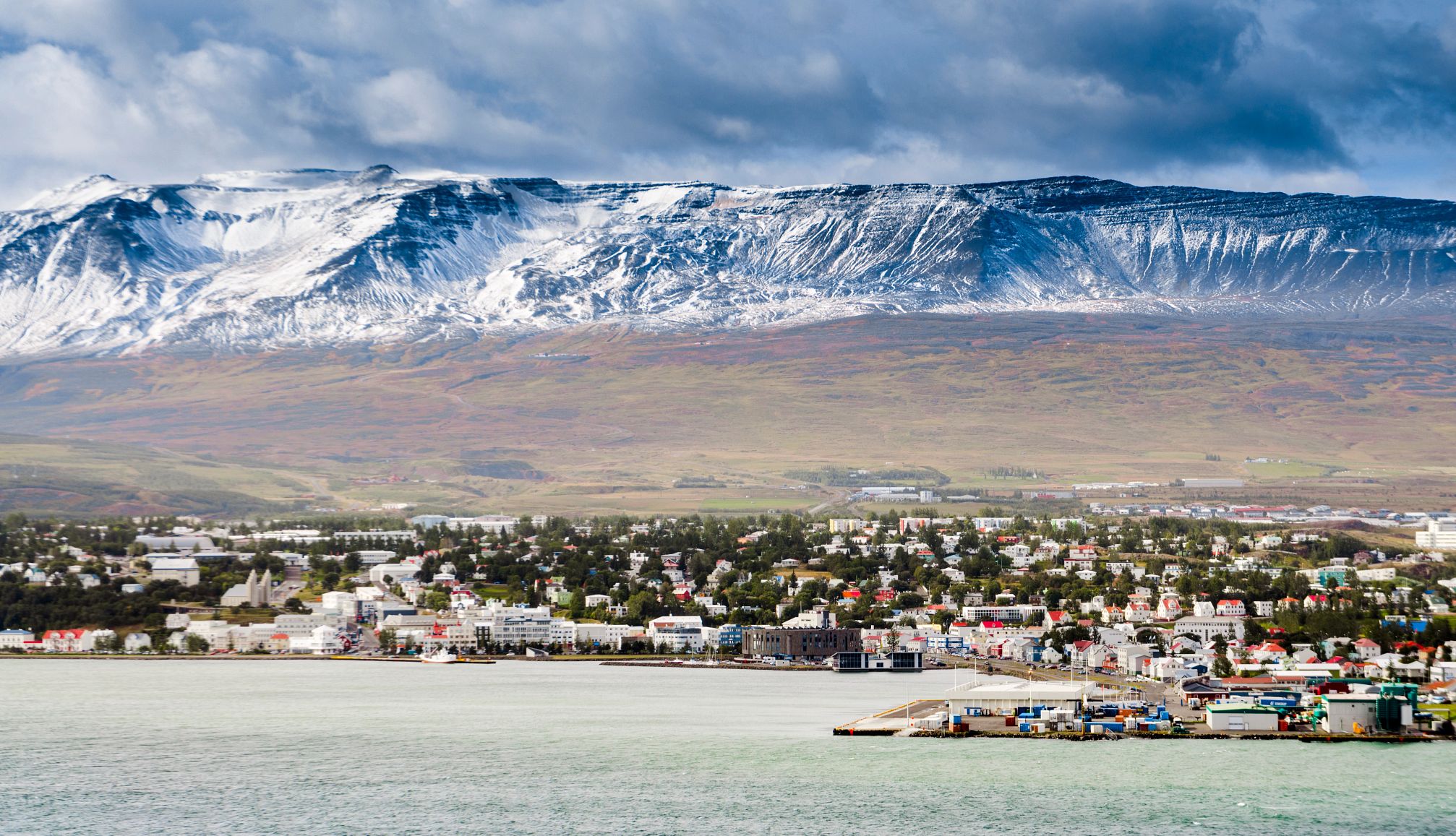 Akureyri Icealand a town near a body of water in the forefront with a mountain behind it
