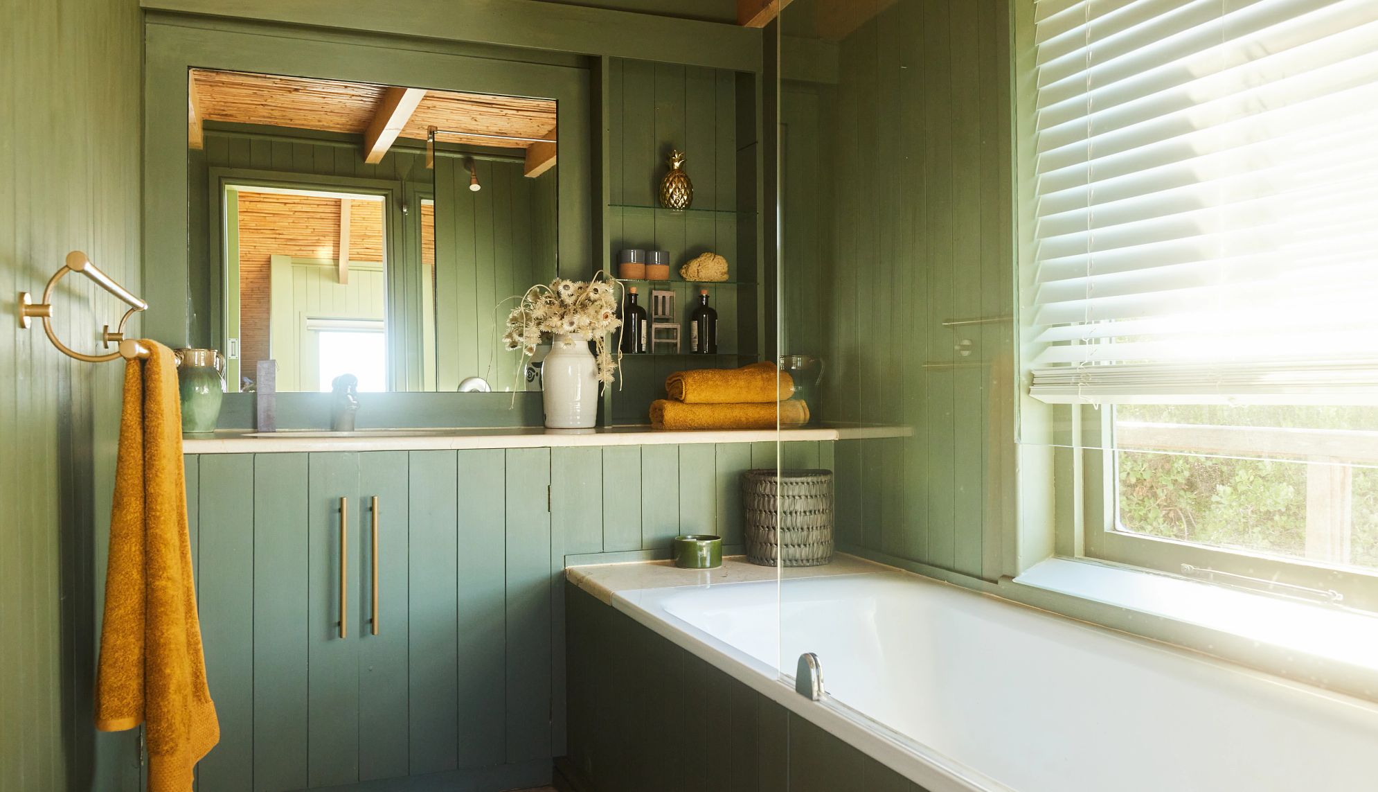 Bañera y mostrador en un cuarto de baño con paredes revestidas de madera verde en una casa de vacaciones