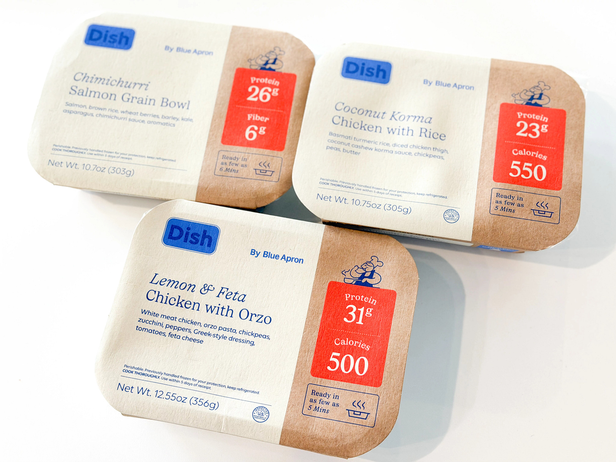 Three Blue Apron prepared meals still packaged on a white countertop