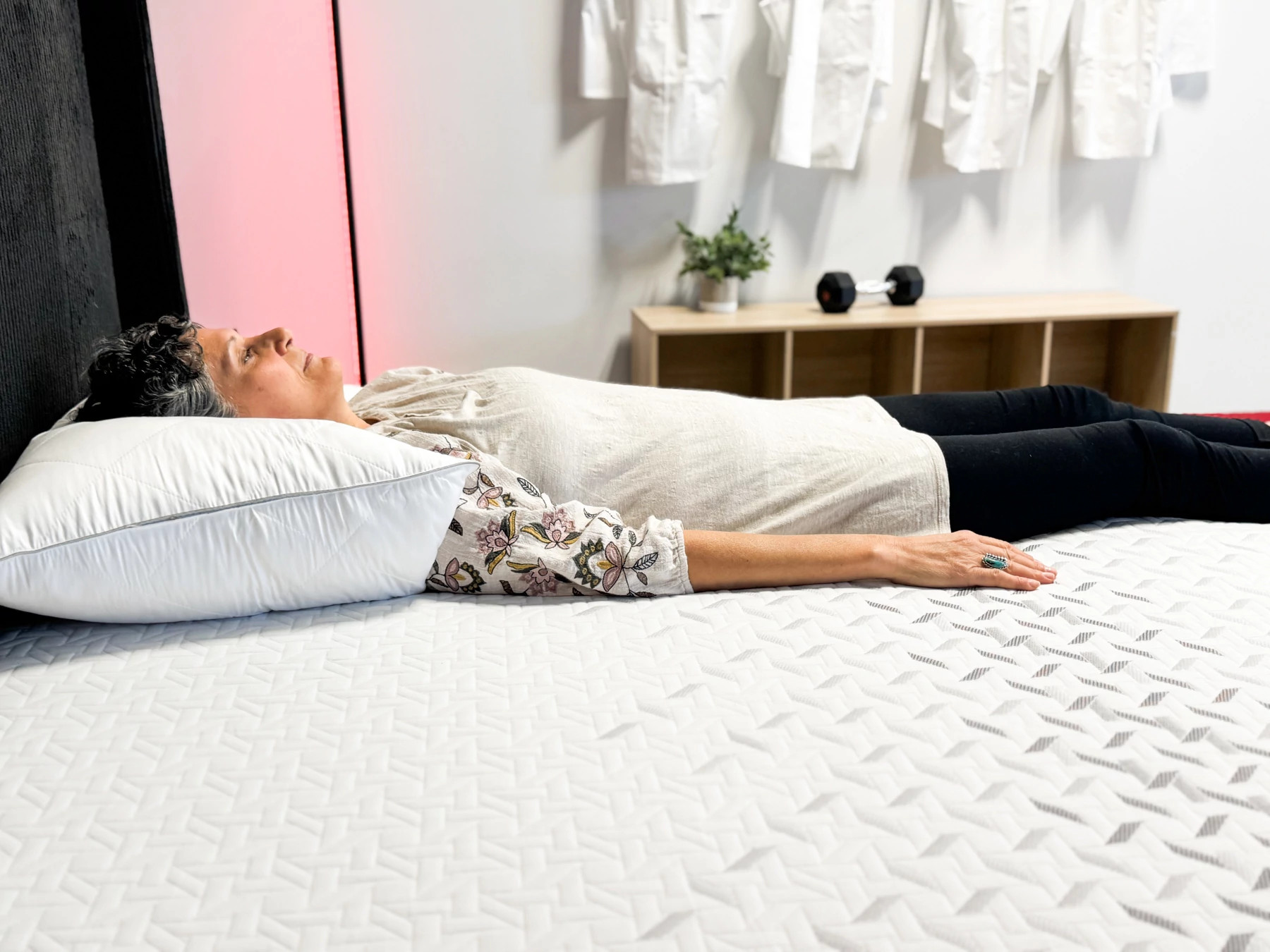 Woman lies on her back on a mattress with her arms at her side.