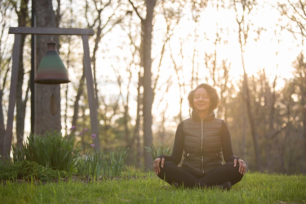 Person meditating cross-legged on grass at a Pennsylvania spa retreat surrounded by trees and garden lanterns