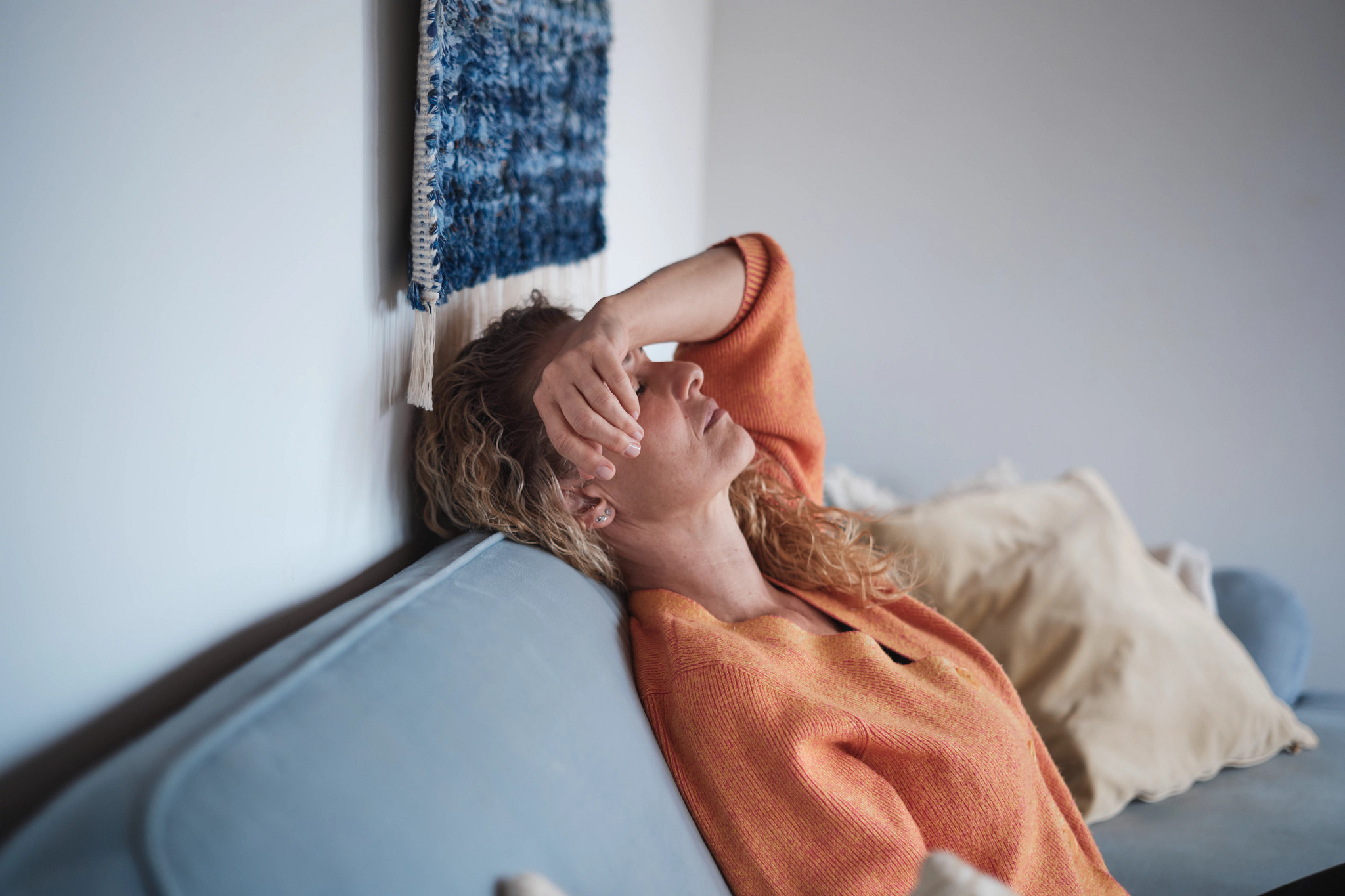 A woman sitting on a couch with her eyes closed and the wrist of her arm resting on her forehead