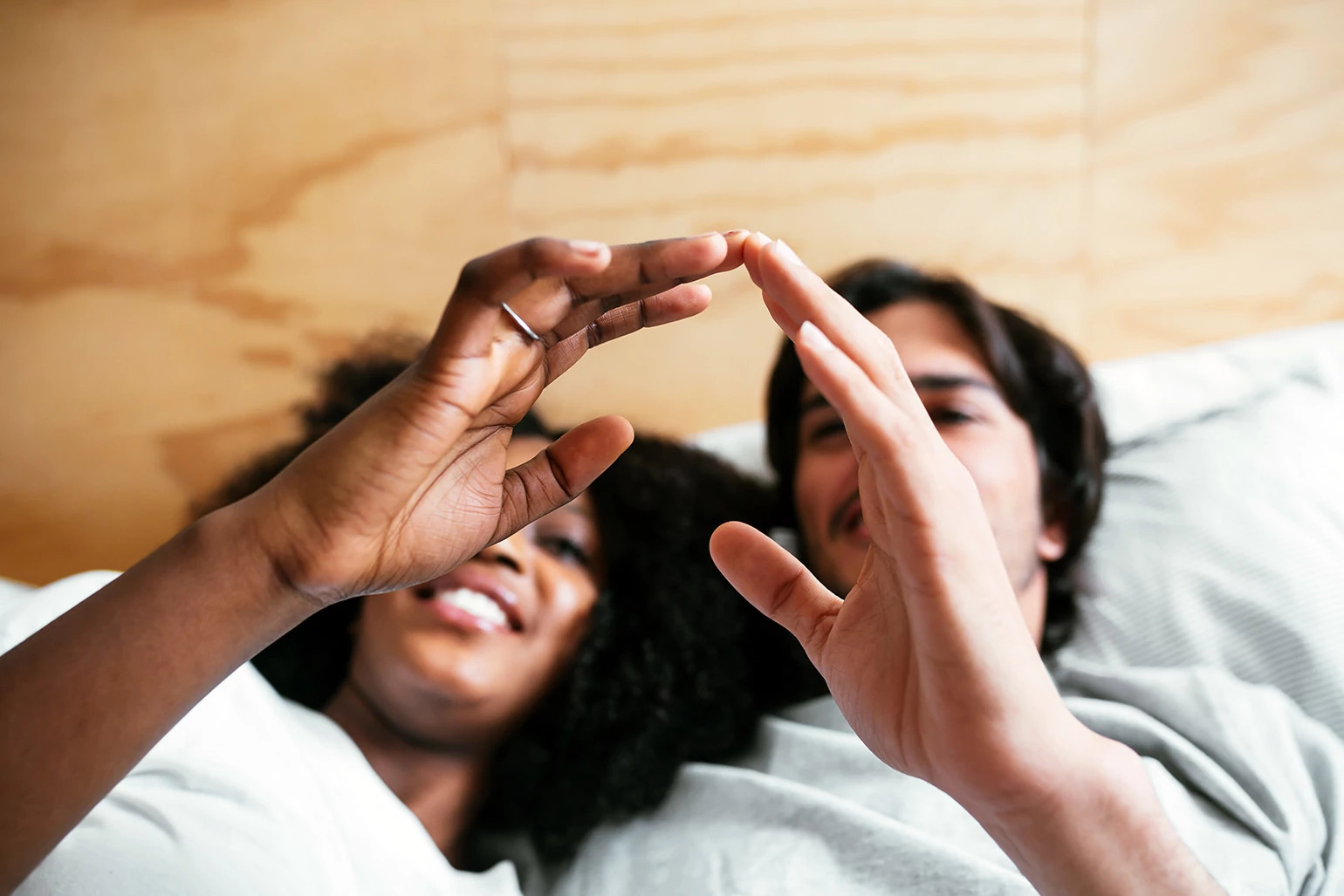 An interracial couple touches fingers while laying in bed.