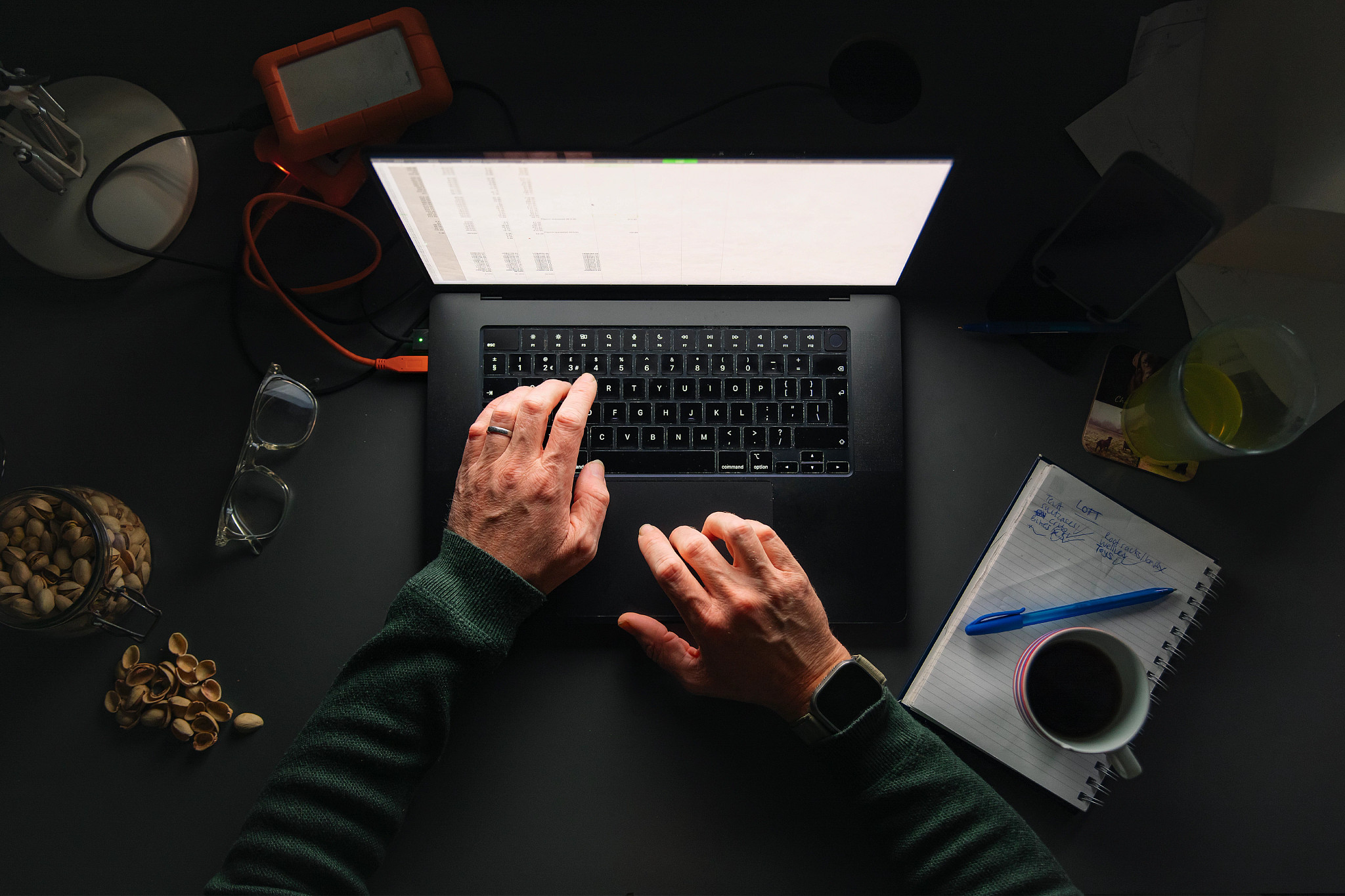 a photo with an overhead view shows an older adult male working on a laptop with a cup of coffee  