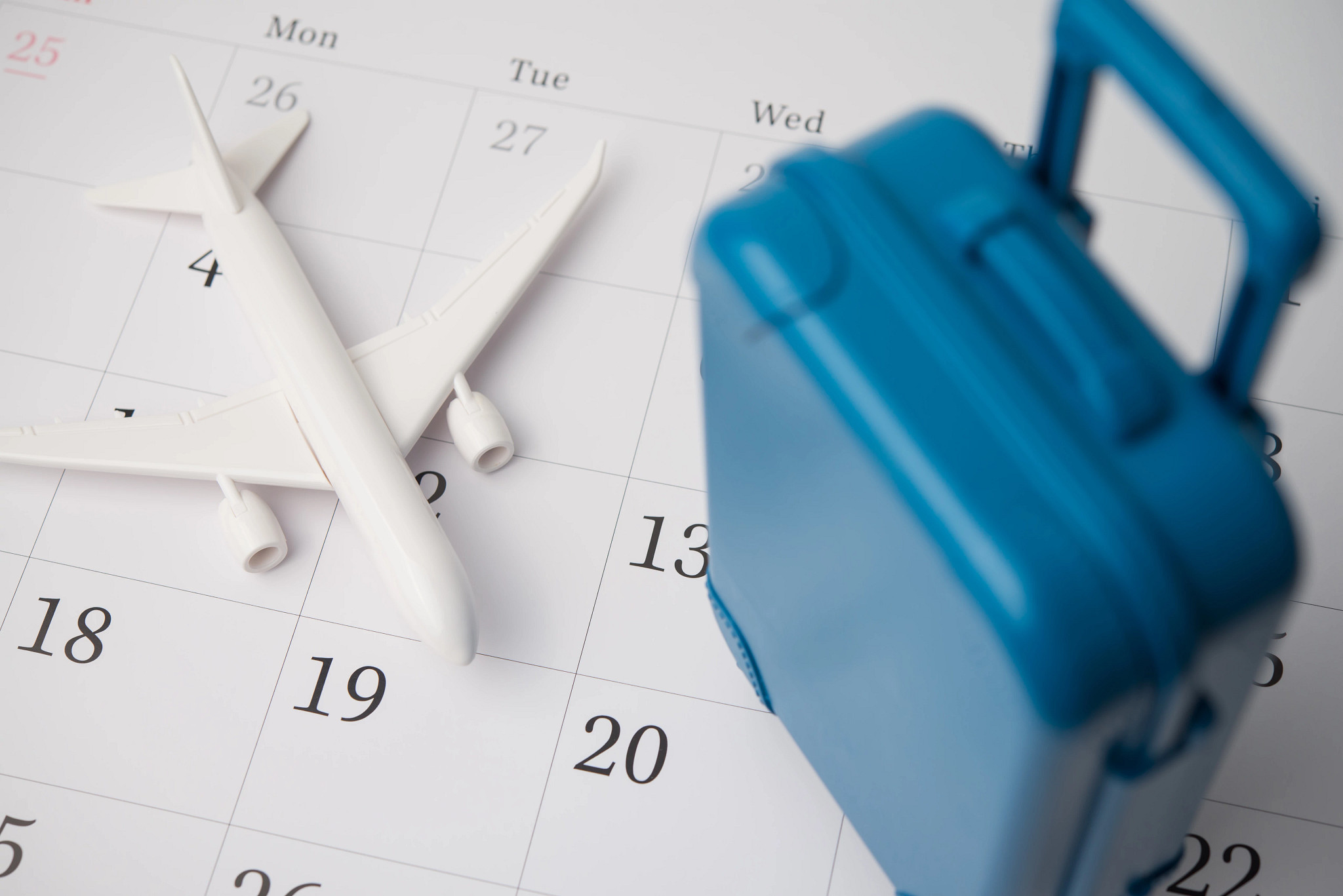 A blue suitcase and an airplane on a blank white calendar background