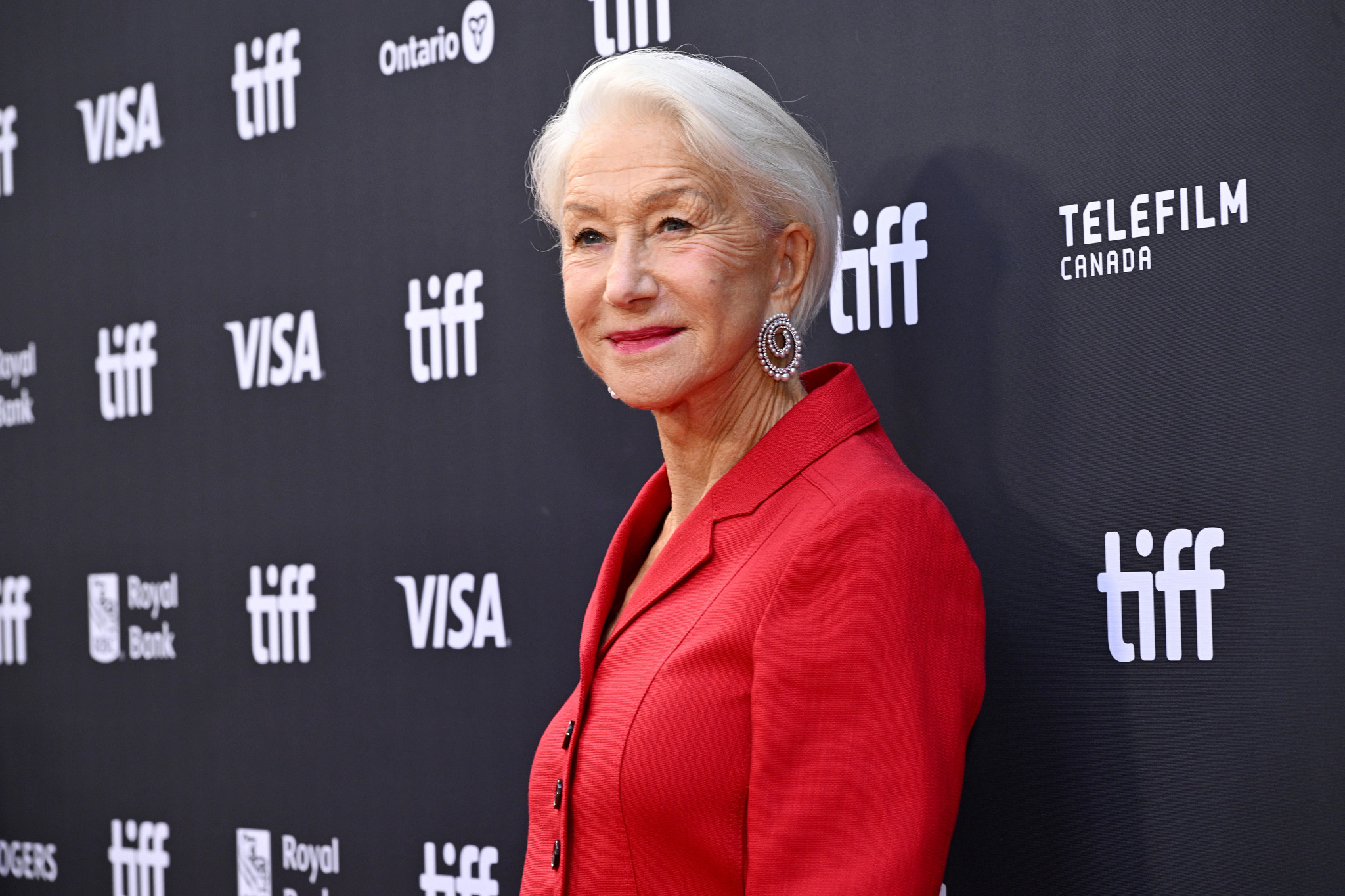 helen mirren posing in a red jacket