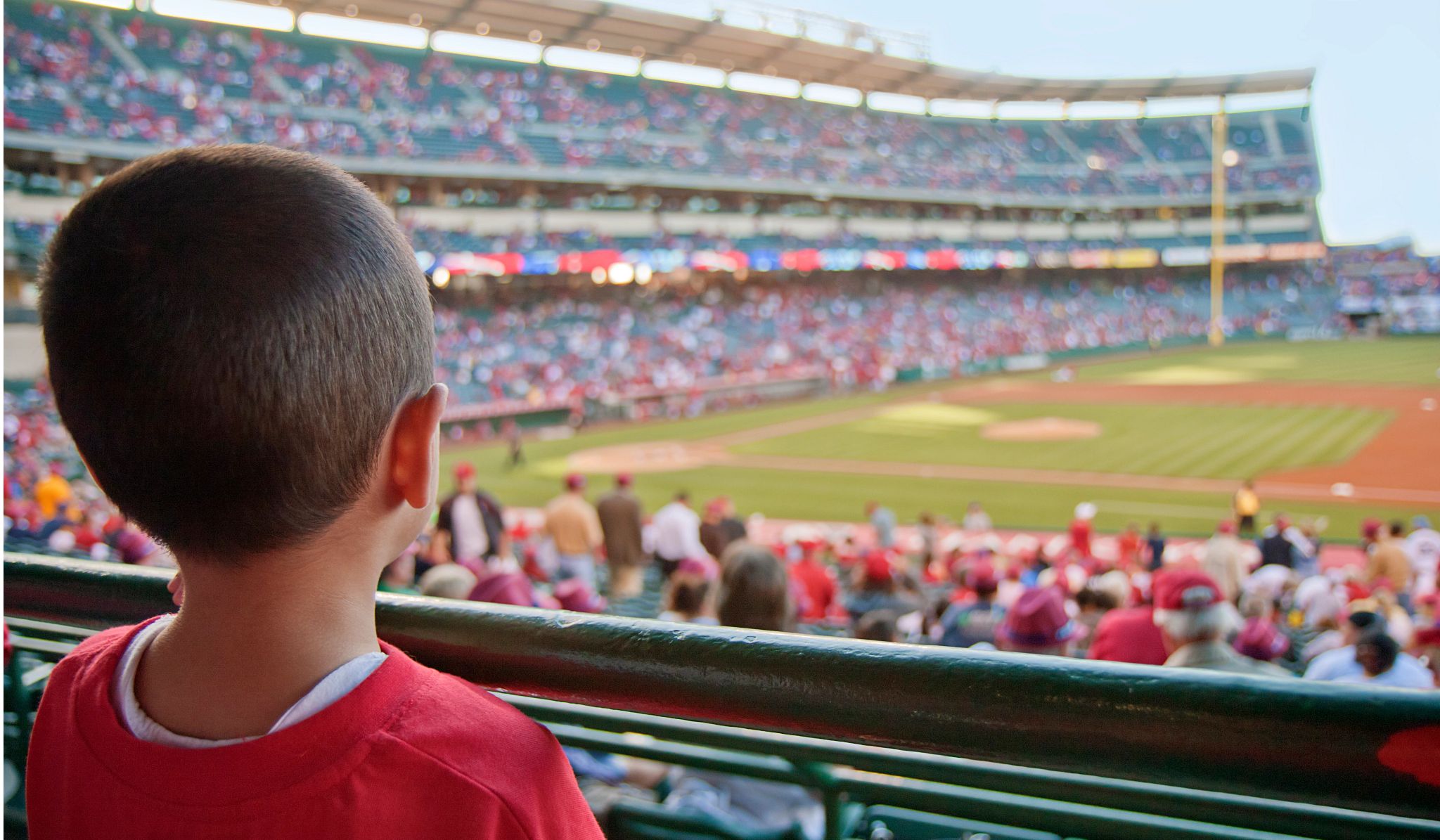 View of a young child at a baseball game, looking out onto the baseball field. View of a young child at a baseball game, looking out onto the baseball field.