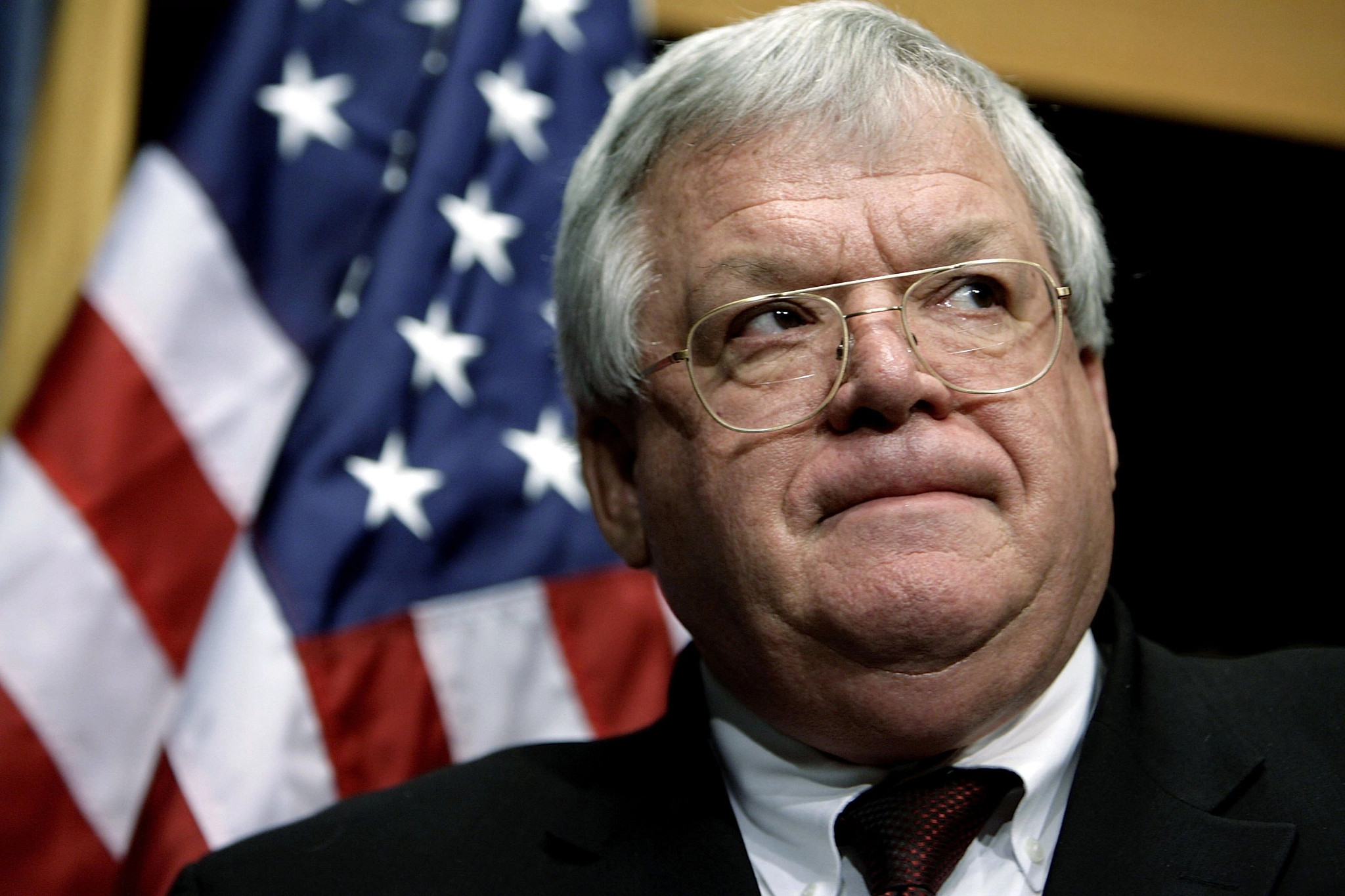 dennis hastert standing near an american flag wearing a suit