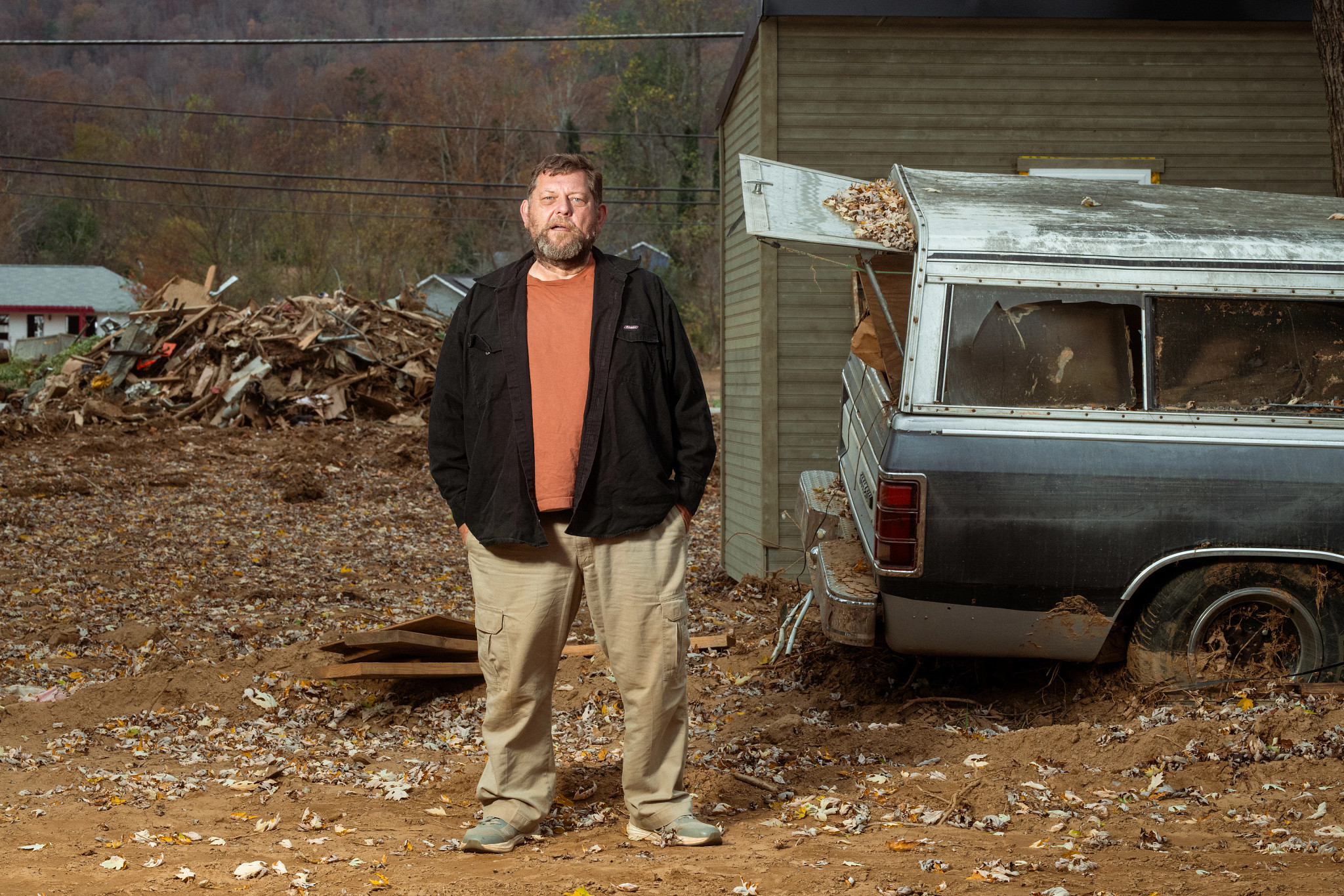 a man stands in his yard, with debris in the background