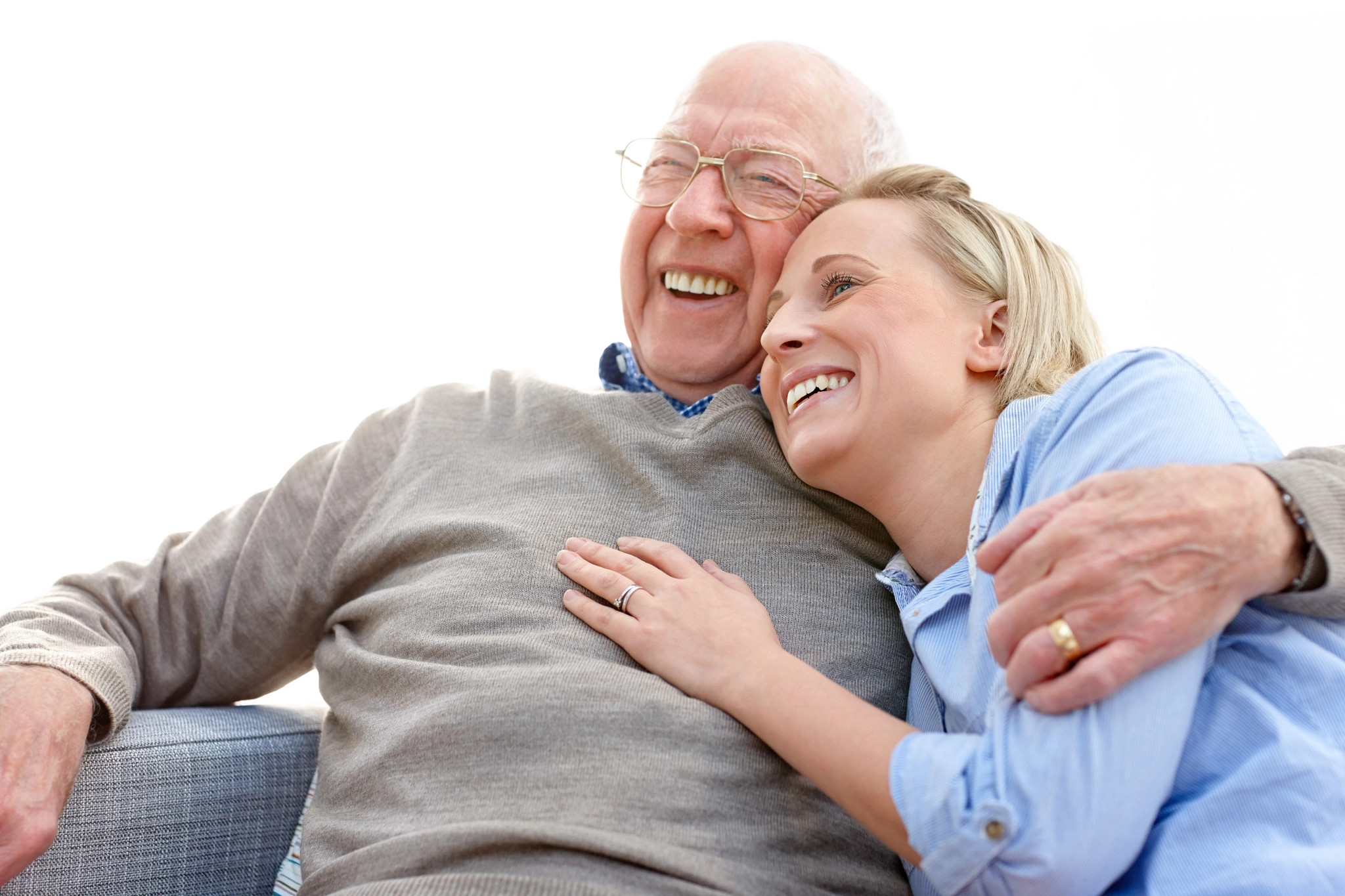 Loving elderly man embracing his daughter looking away smiling while sitting on sofa
