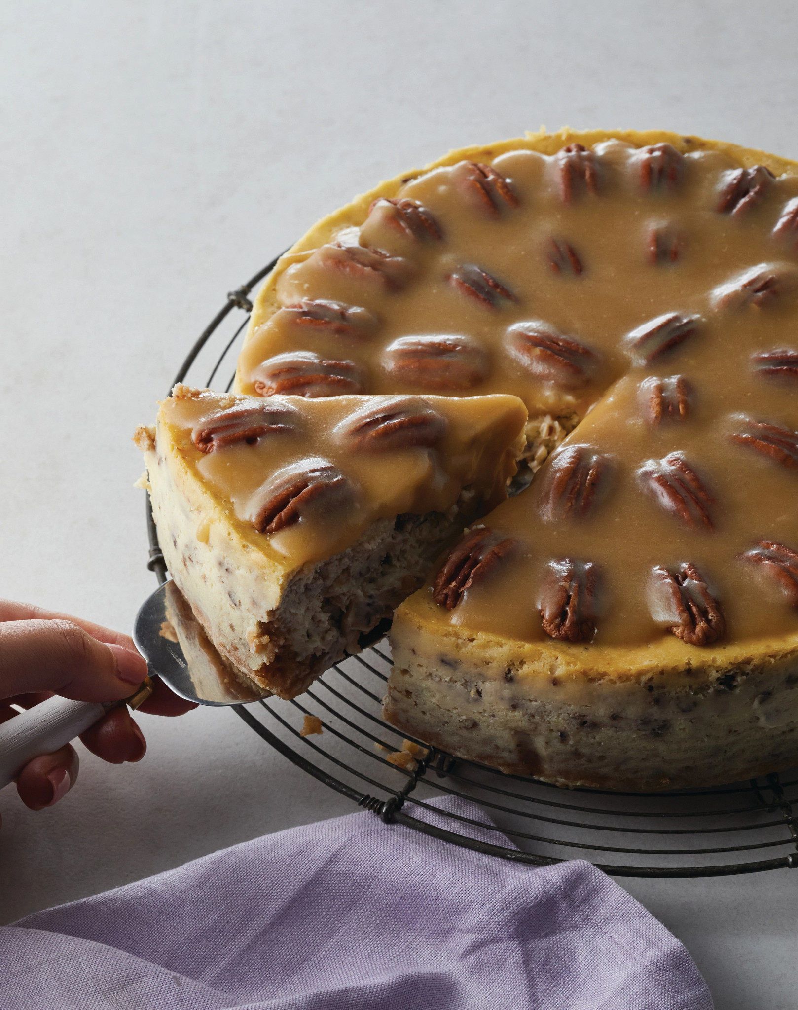 a close-up view of a person serving a slice of butter pecan cheesecake