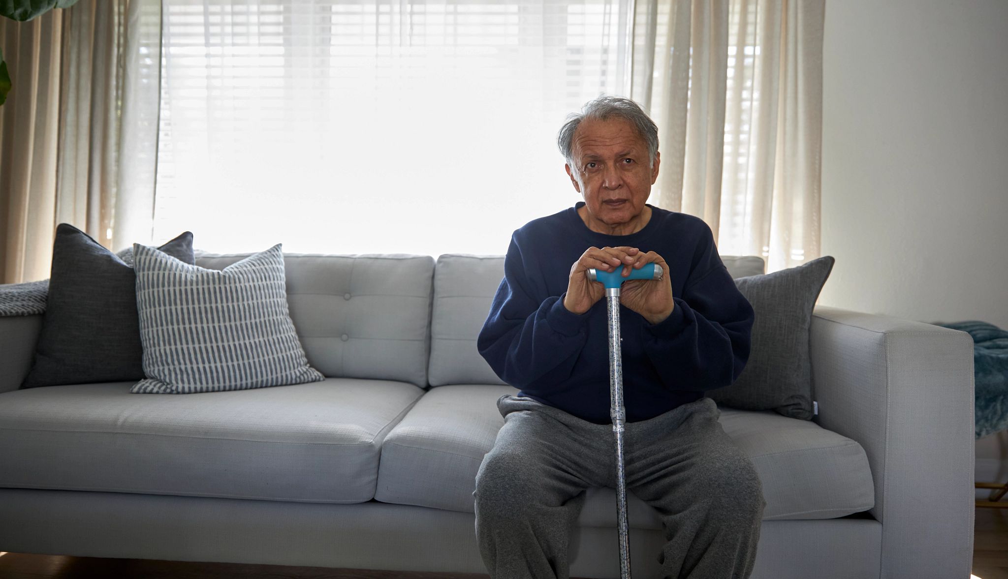Portrait of senior man with cane sitting on sofa at home