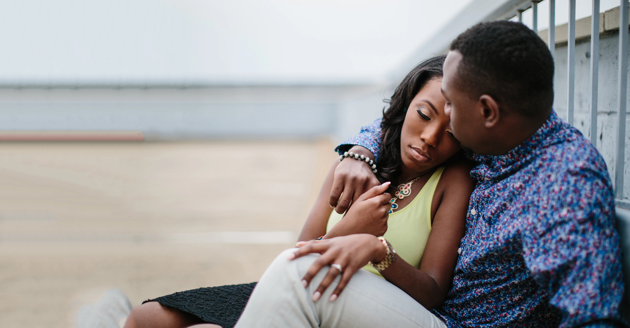 A man and a woman sit holding one another on top of a parking garage.