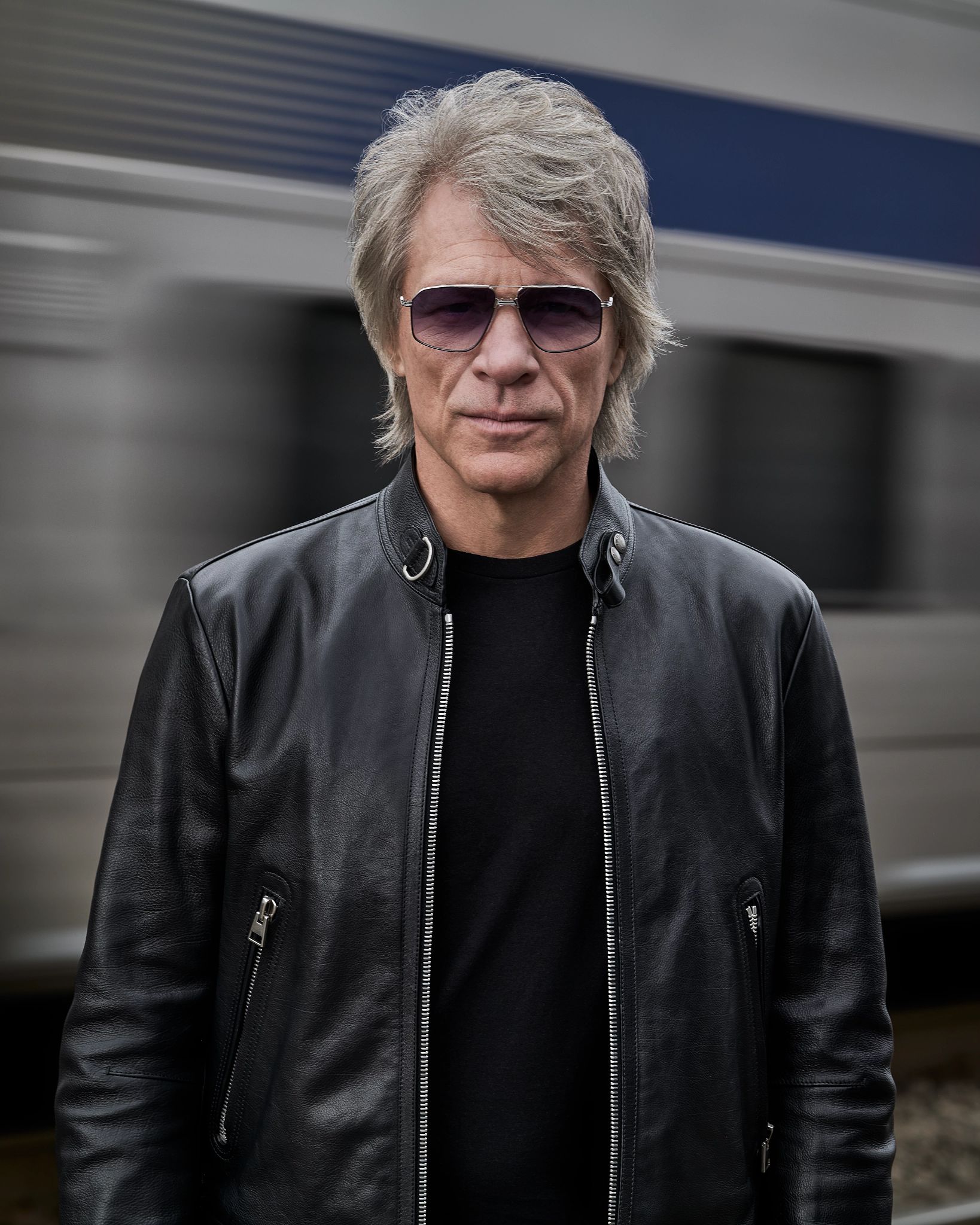 Jon Bon Jovi wearing sunglasses with a vehicle passing behind him