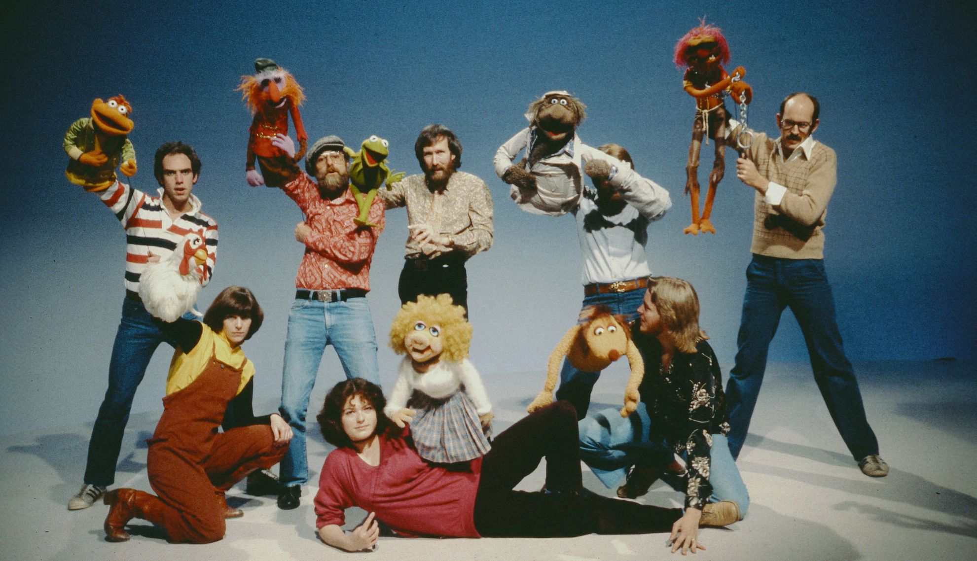 Jim Henson and other Muppet puppeteers holding their Sesame Street puppet characters in the air