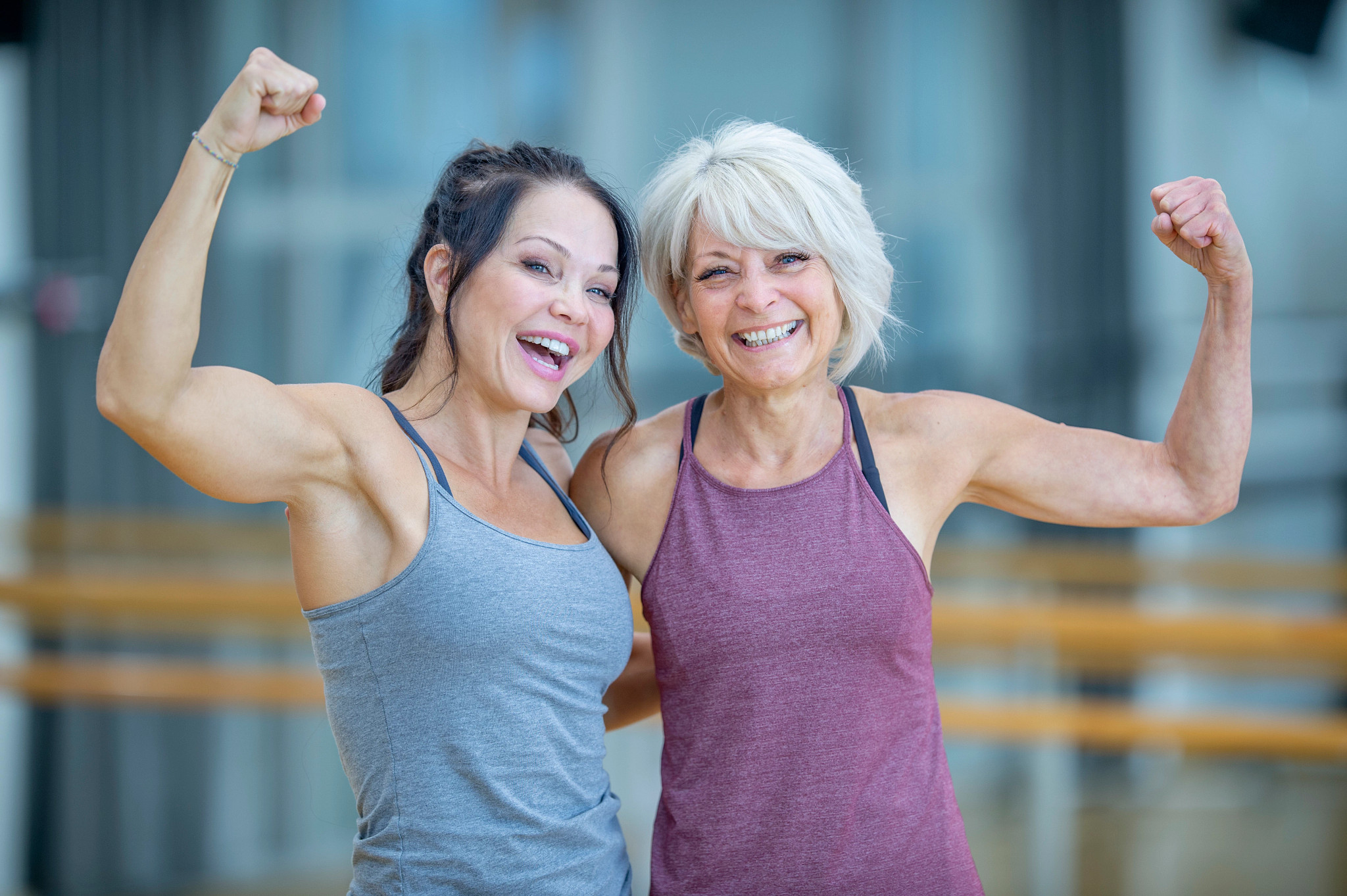 two people smiling, wearing activewear and showing their arms in a bicep curl
