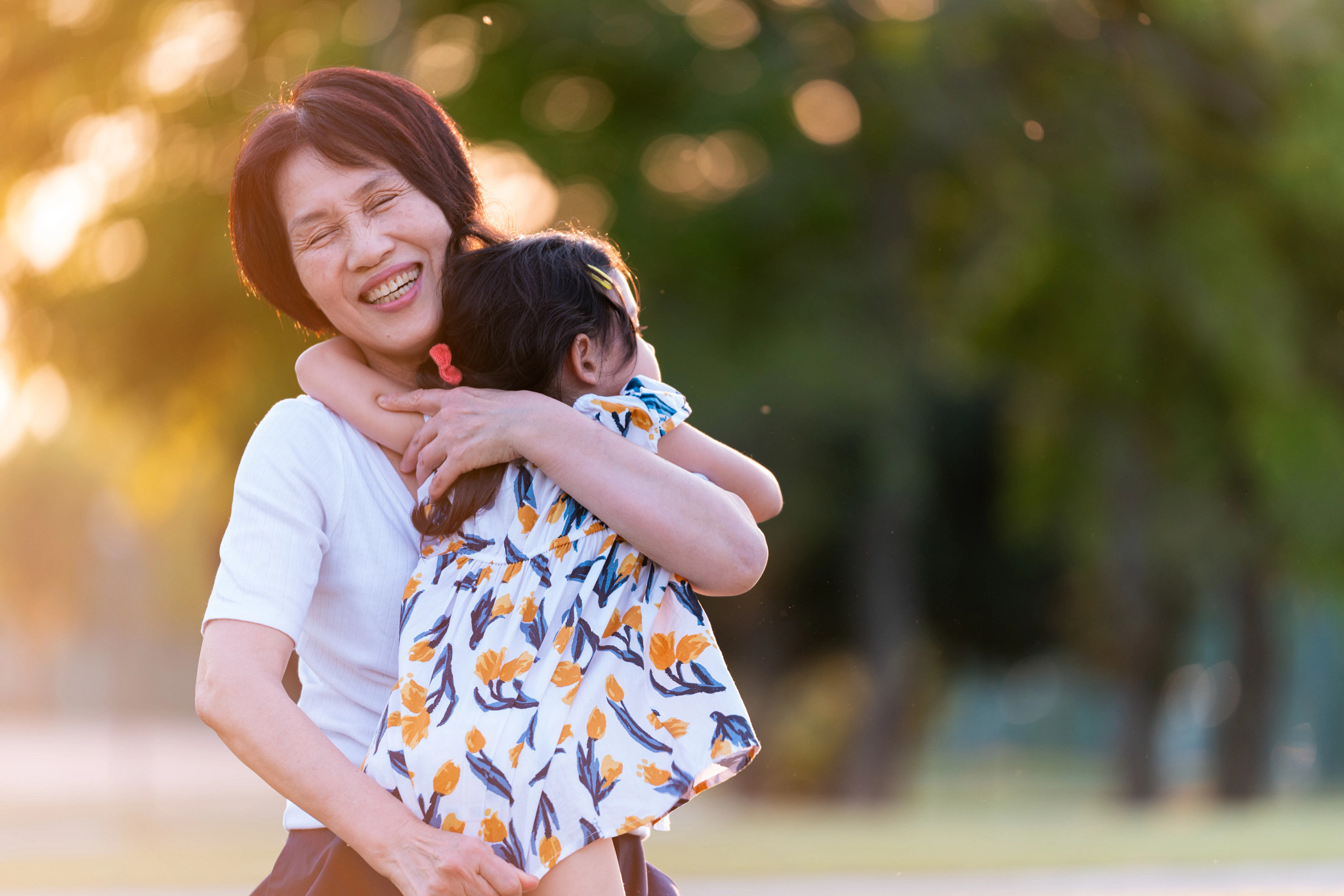 Grandmother and granddaughter hugging outdoors in the park.