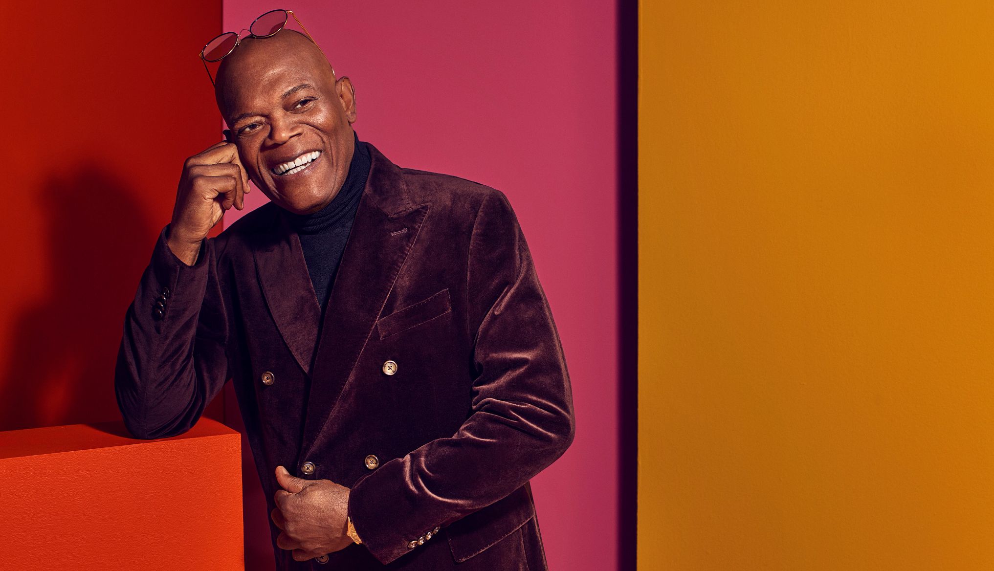 Samuel L. Jackson Samuel L. Jackson smiles with glasses lying on the top of head while wearing a purple suede jacket