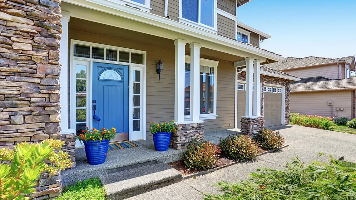 American Home Shield front of house tan with blue door and stone accents bright blue sky