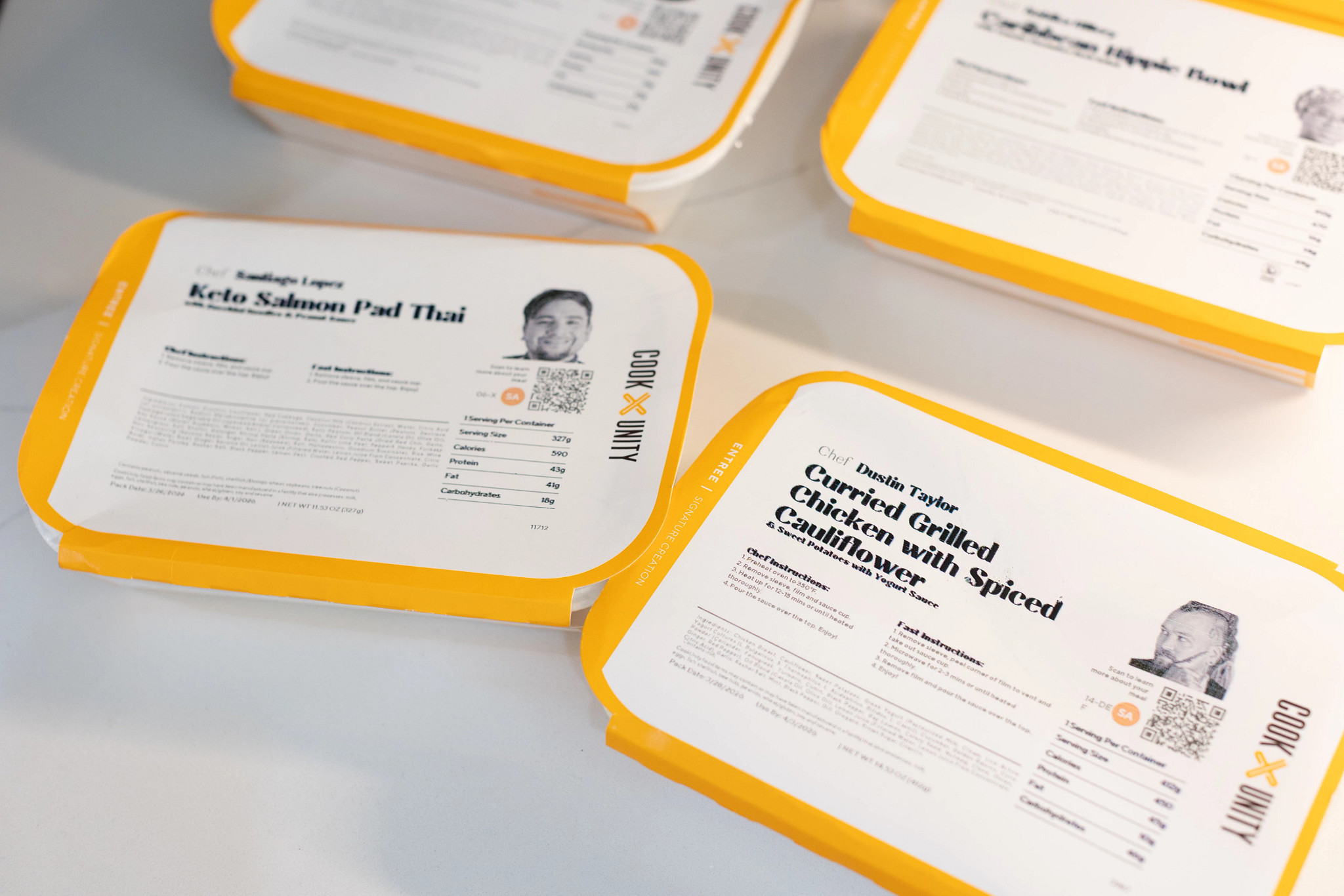 Four CookUnity meals inside their packaging on a white table