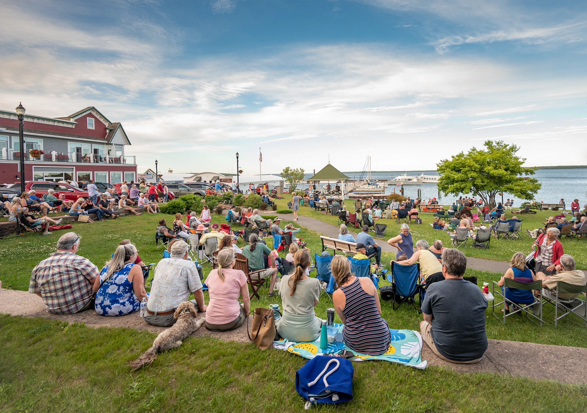 a large crowd sitting in a grassy area near a lake