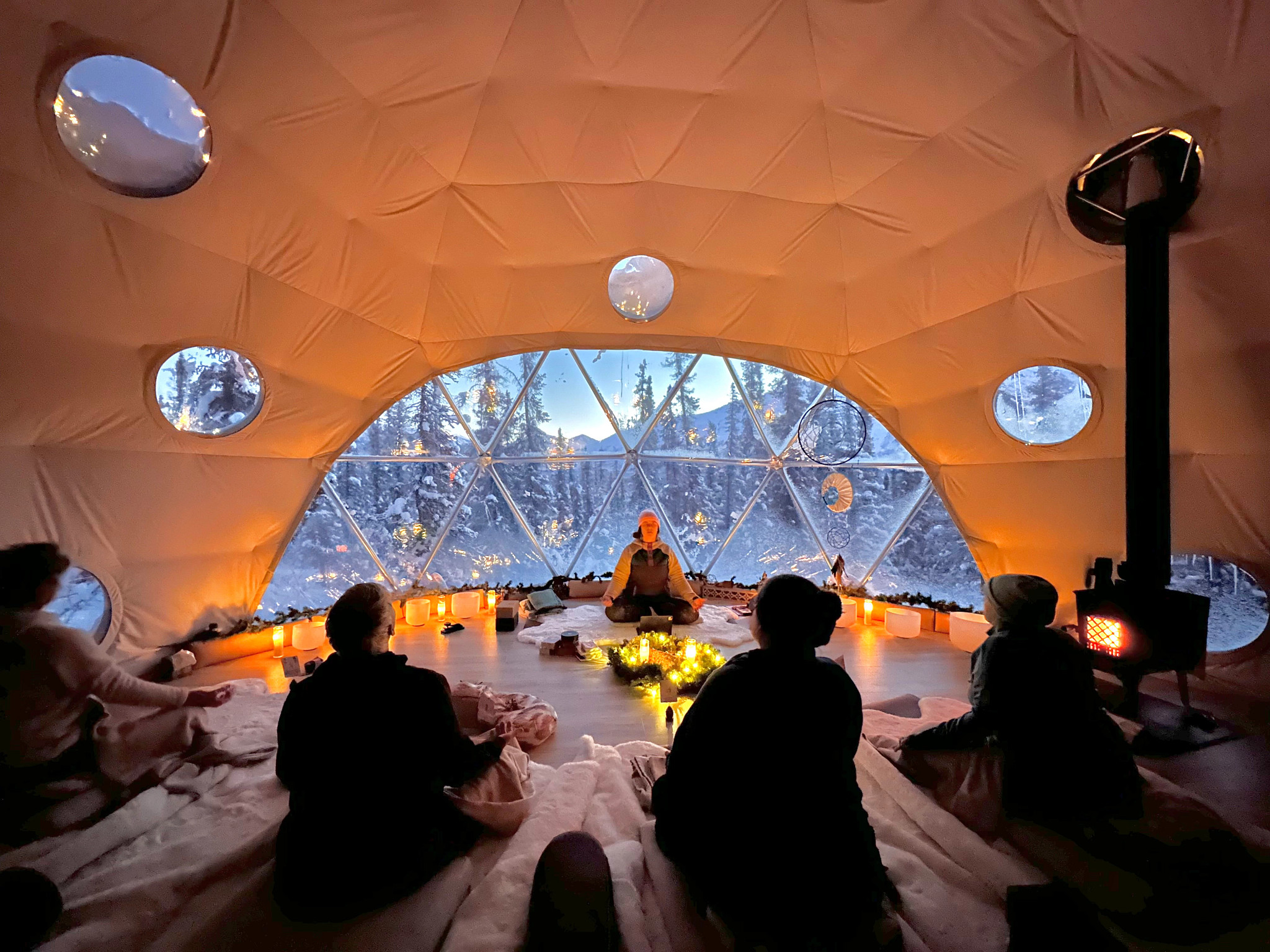 people practicing yoga in an igloo-shaped tent with snow-covered trees in the background