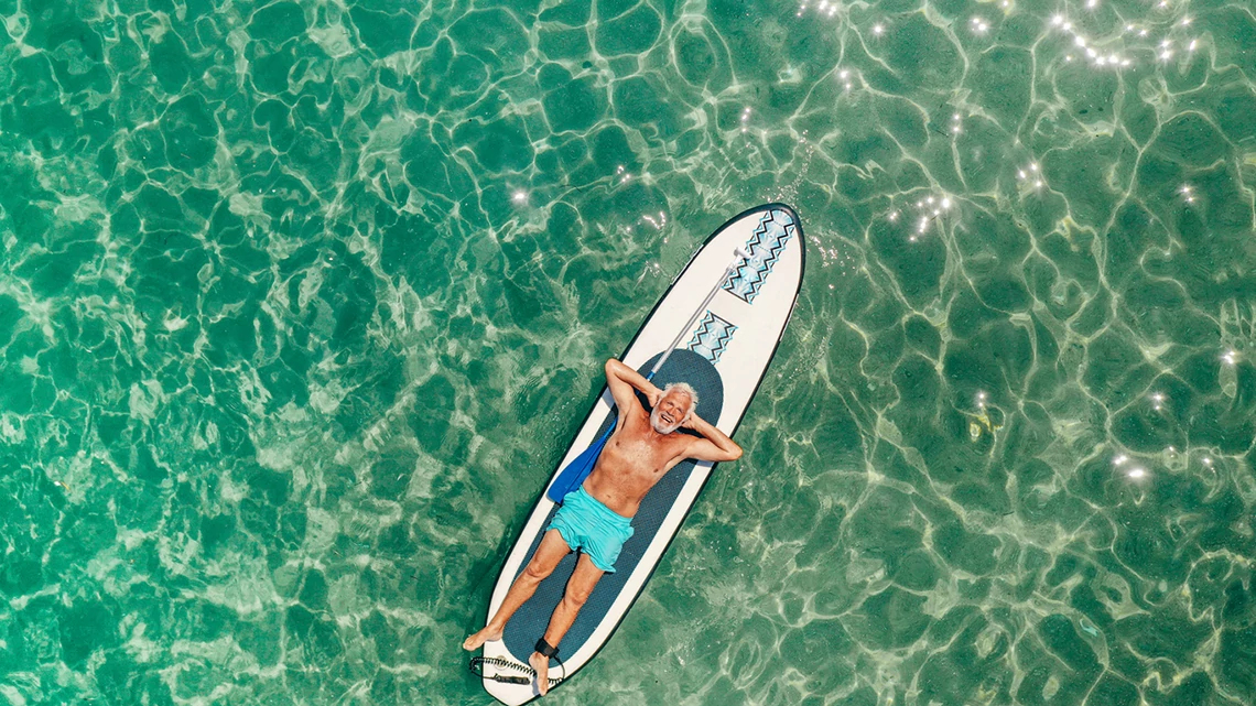 senior man stretched out on a paddleboard in sea glass green water