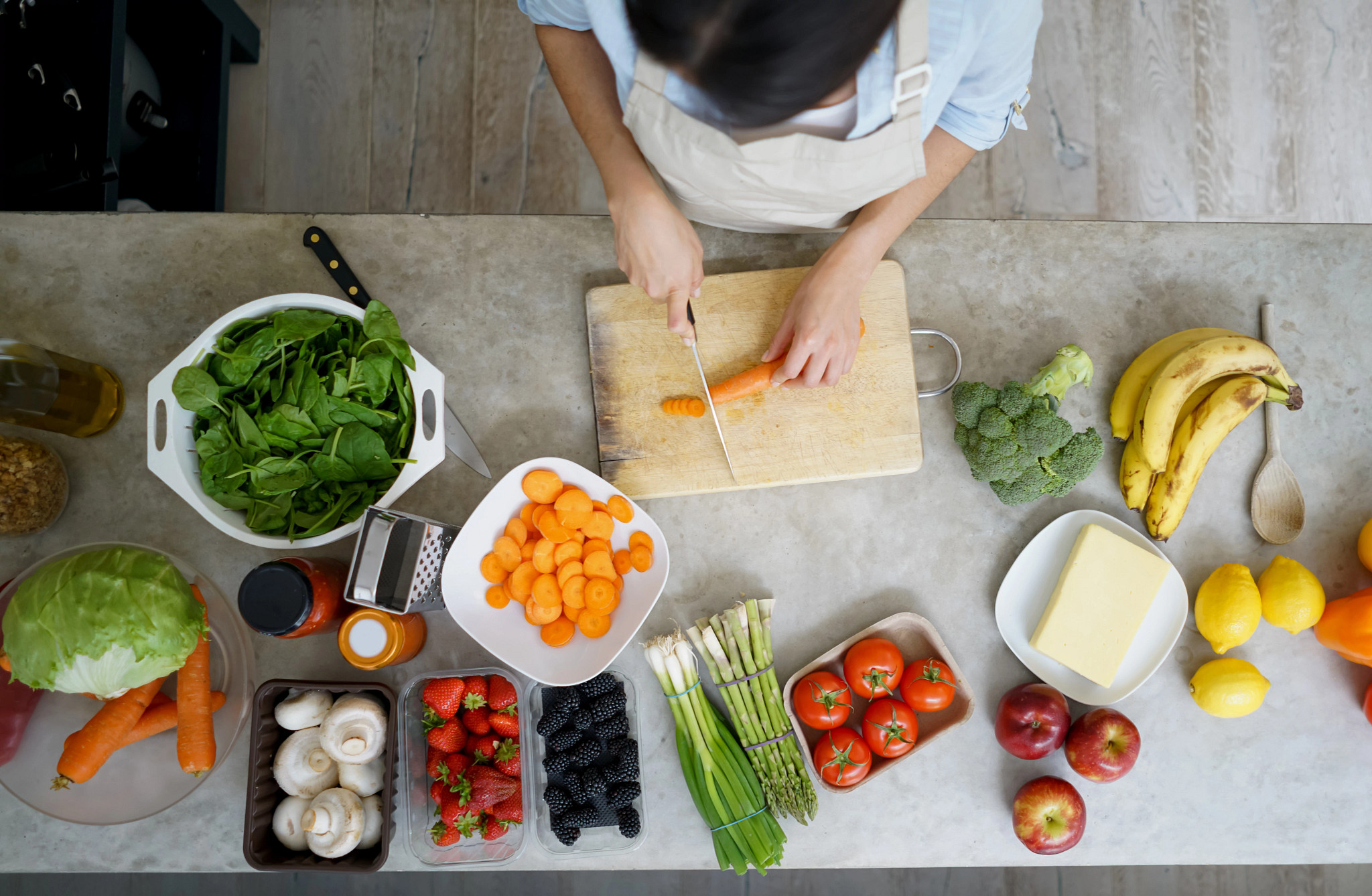 a table with many different ingredients like tomatoes, carrots, broccoli and more with someone preparing dinner.