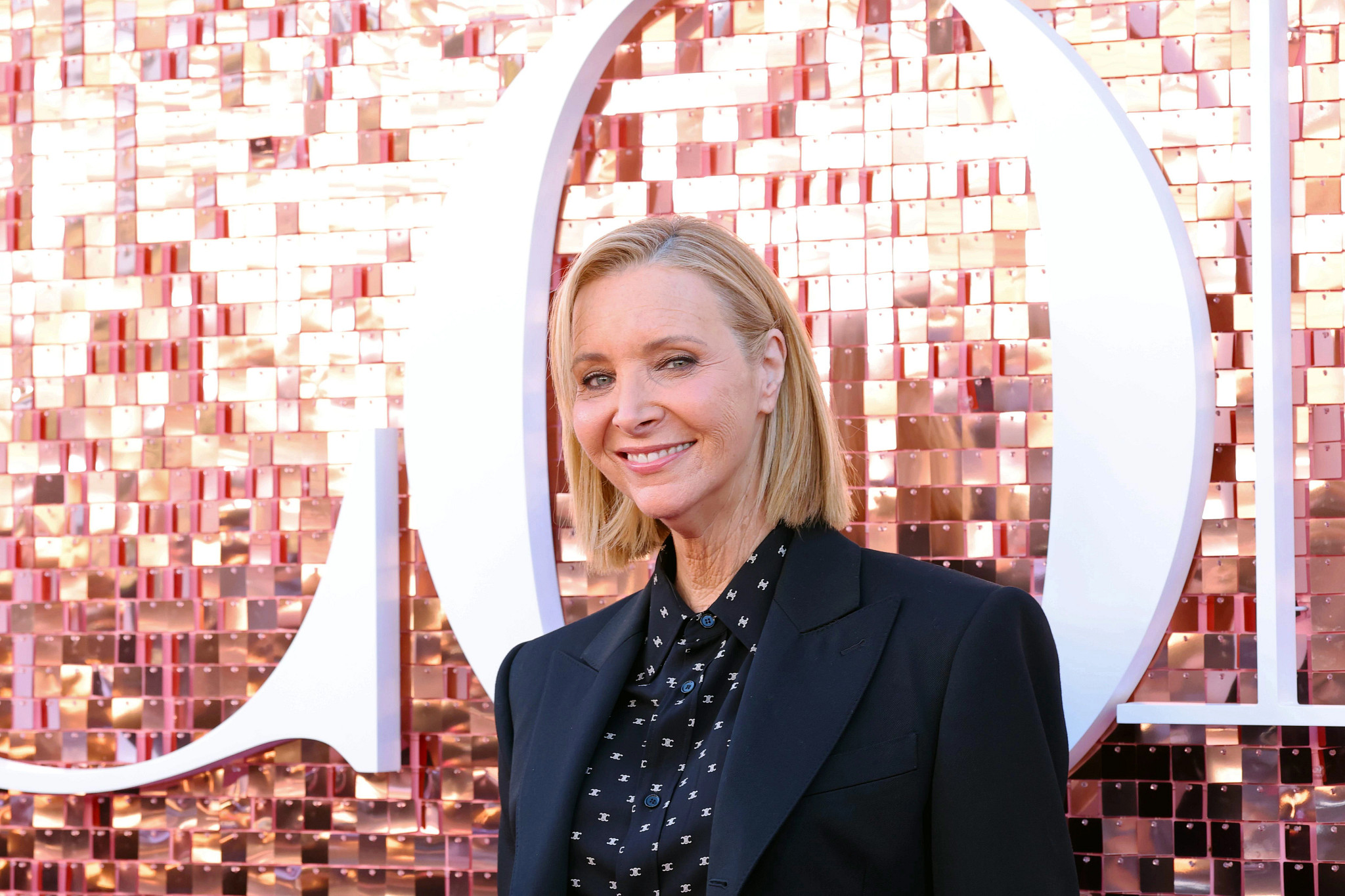 lisa kudrow smiling, wearing a box bob haircut and a black jacket