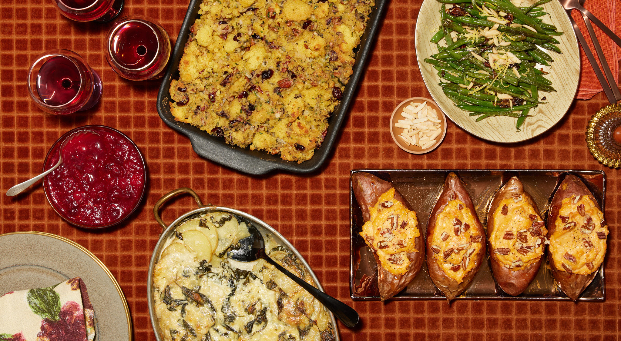Overhead photo of a Thanksgiving meal featuring stuffing, cranberry sauce, green beans with sliced almonds, twice-baked sweet potatoes, and creamy potato casserole on a fall-themed table