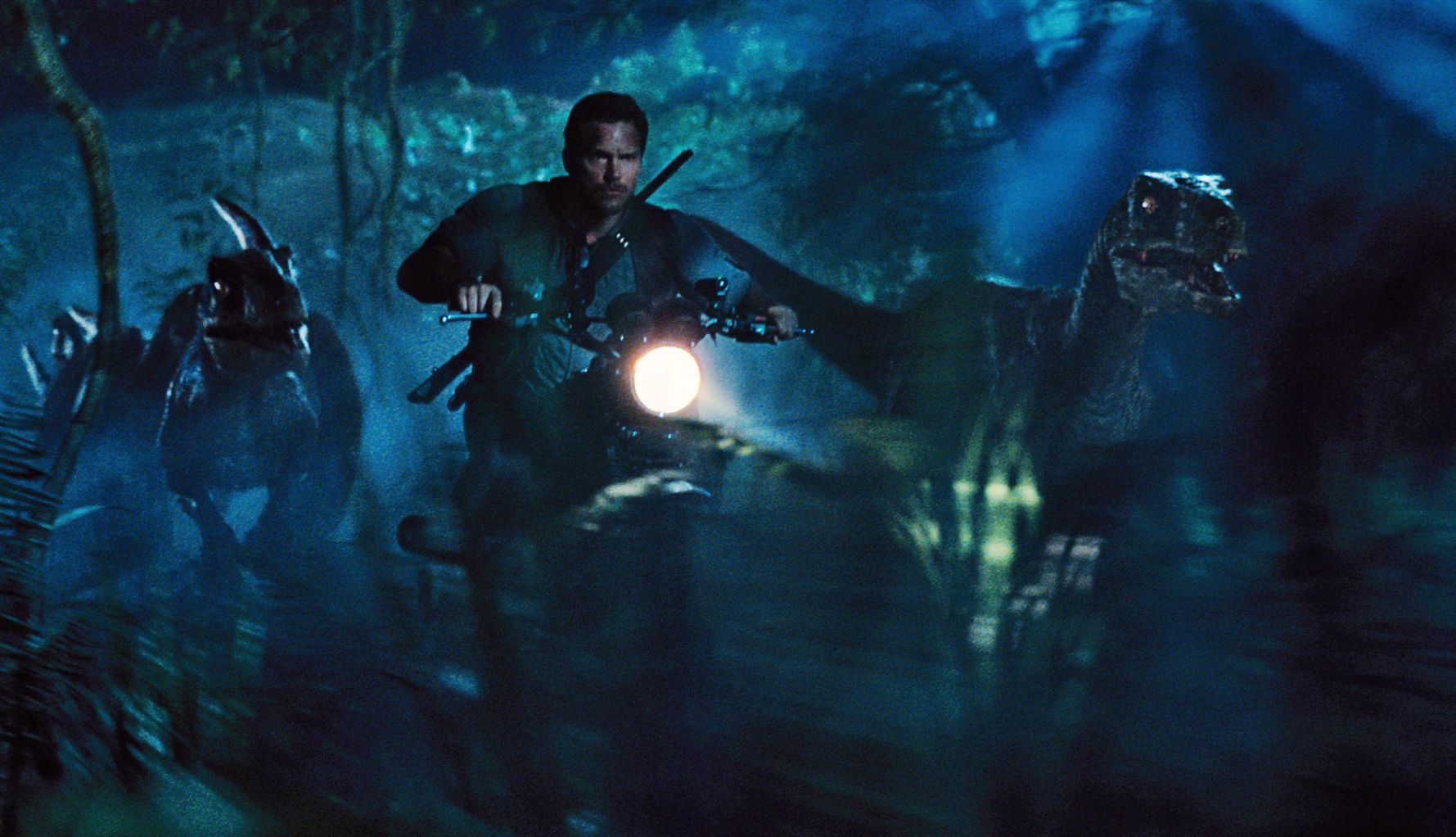 All the ‘Jurassic’ Movies, Ranked! chris pratt riding a motorcycle while flanked by galloping velociraptors