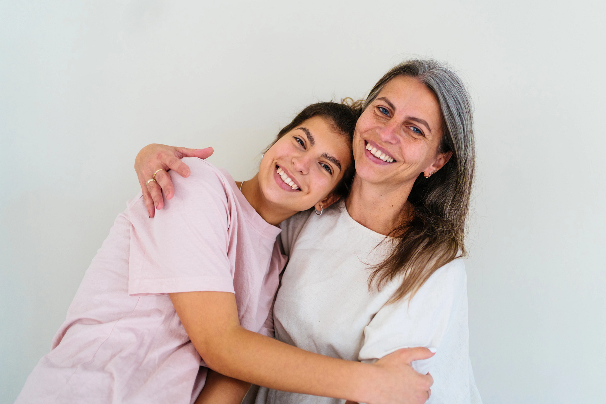 A mother and her teenage daughter smiling and hugging each other.
