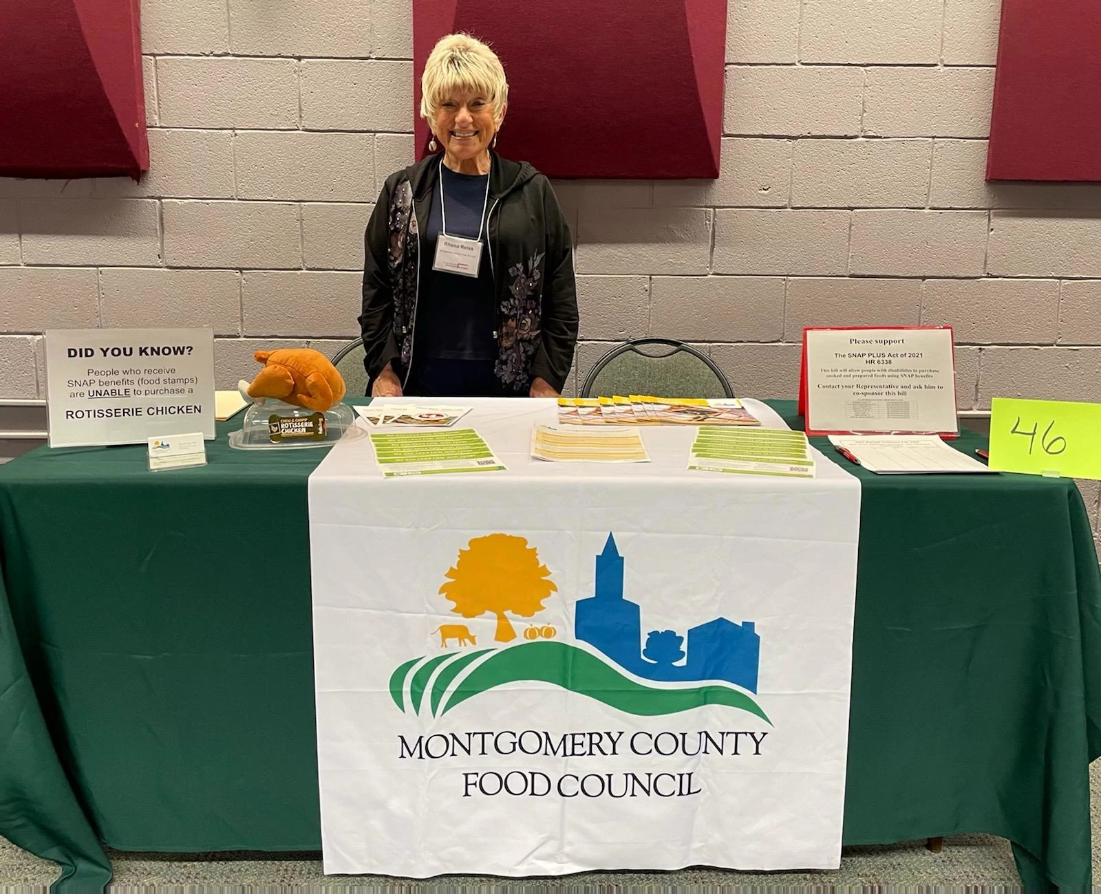 a woman stands behind a table for the montgomery county food council