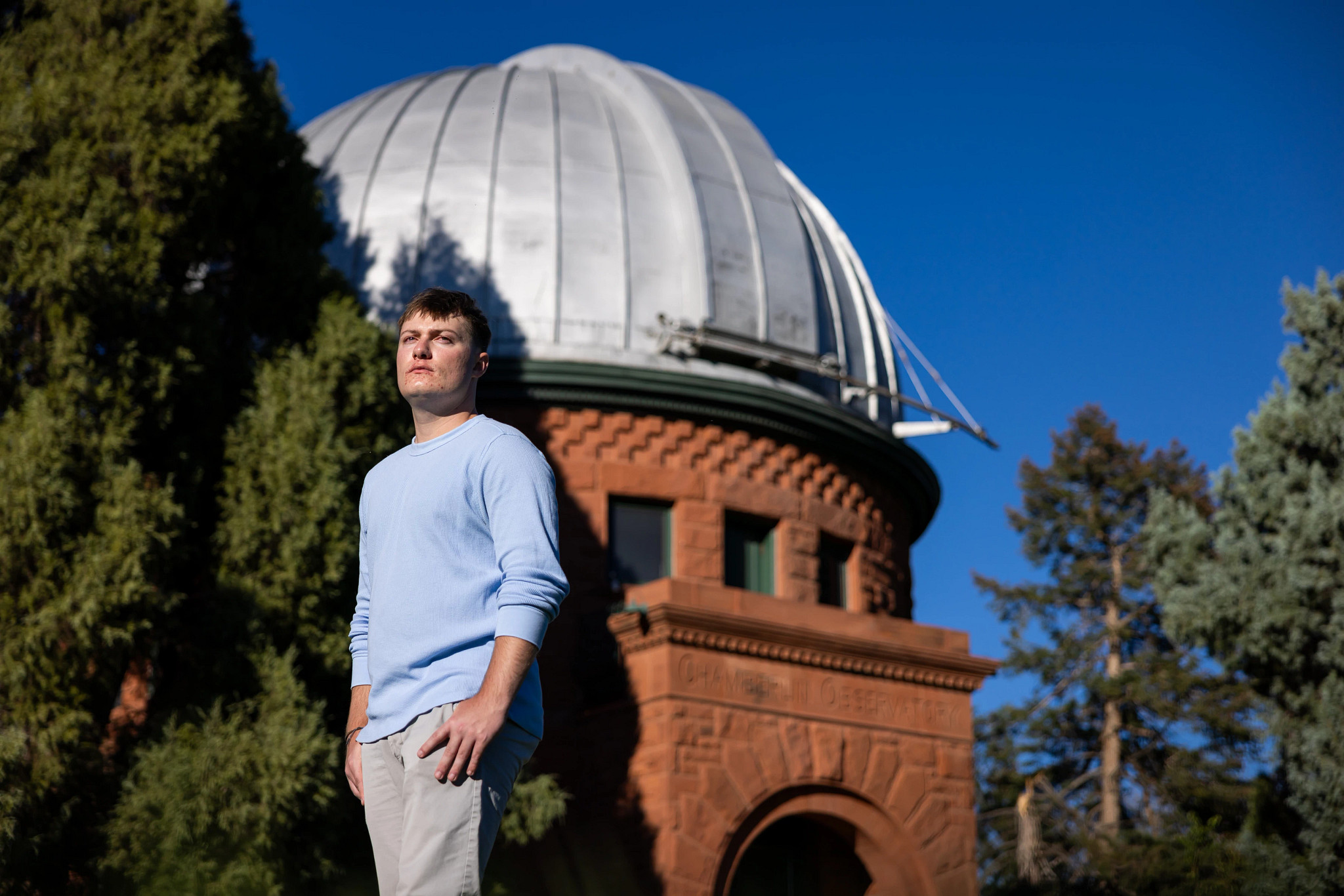 Evan Clark stands in front of the historic stone building and large white dome of the Chamberlin Observatory.