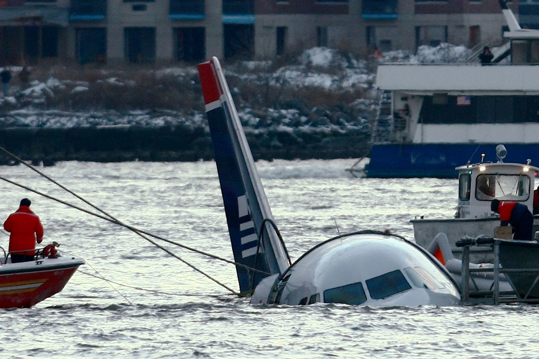 The partially submerged nose and tail of the US Airways Flight 1549 airplane in the cold Hudson River, surrounded by rescue boats and recovery lines.