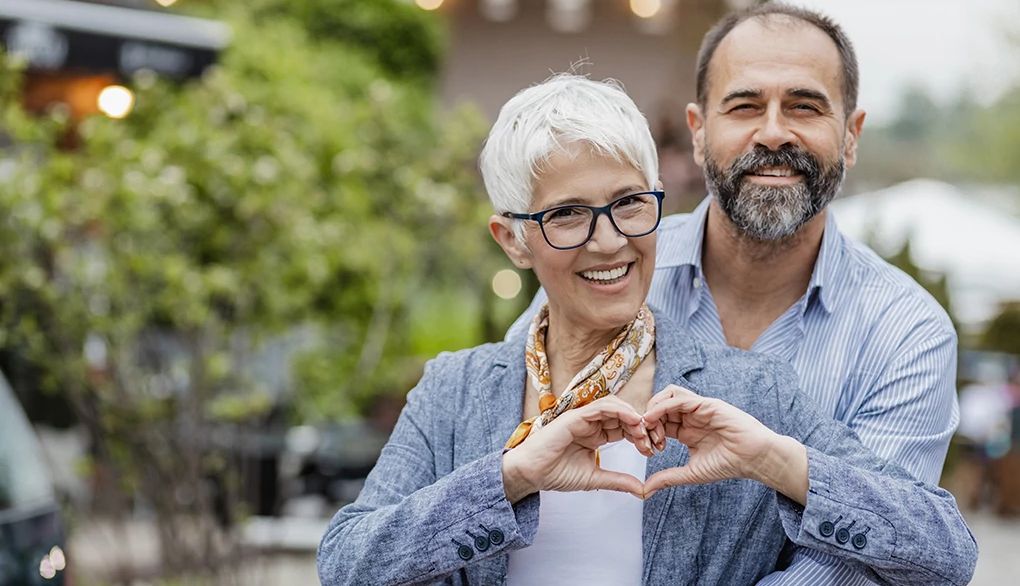 Being kind may lift your spirit A woman making a heart shape with her hands with a man behind her
