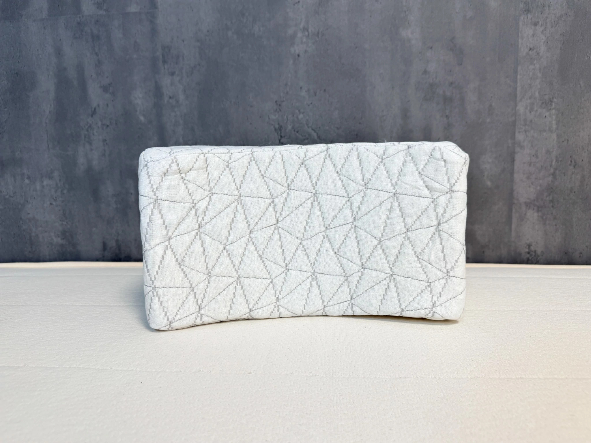 A white Coop Adjustable Knee Pillow displayed in front of a gray wall