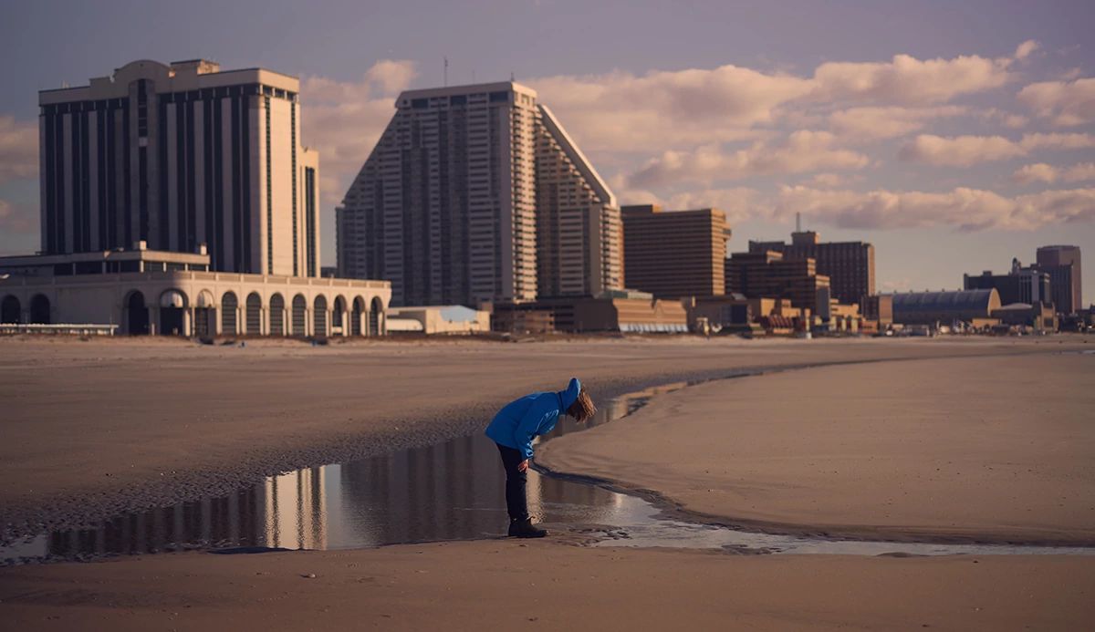 City skyline against a sandy beach, with a person in a blue jacket