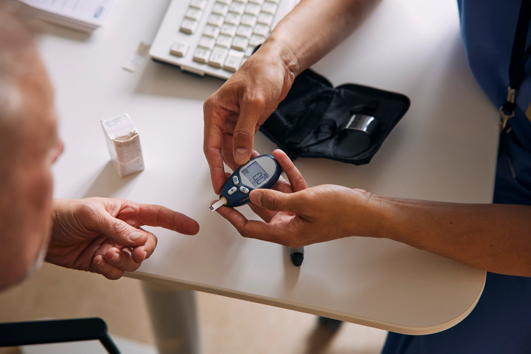 a top down view of a medical technician perparing to use a glucometer to check another persons blood glucose