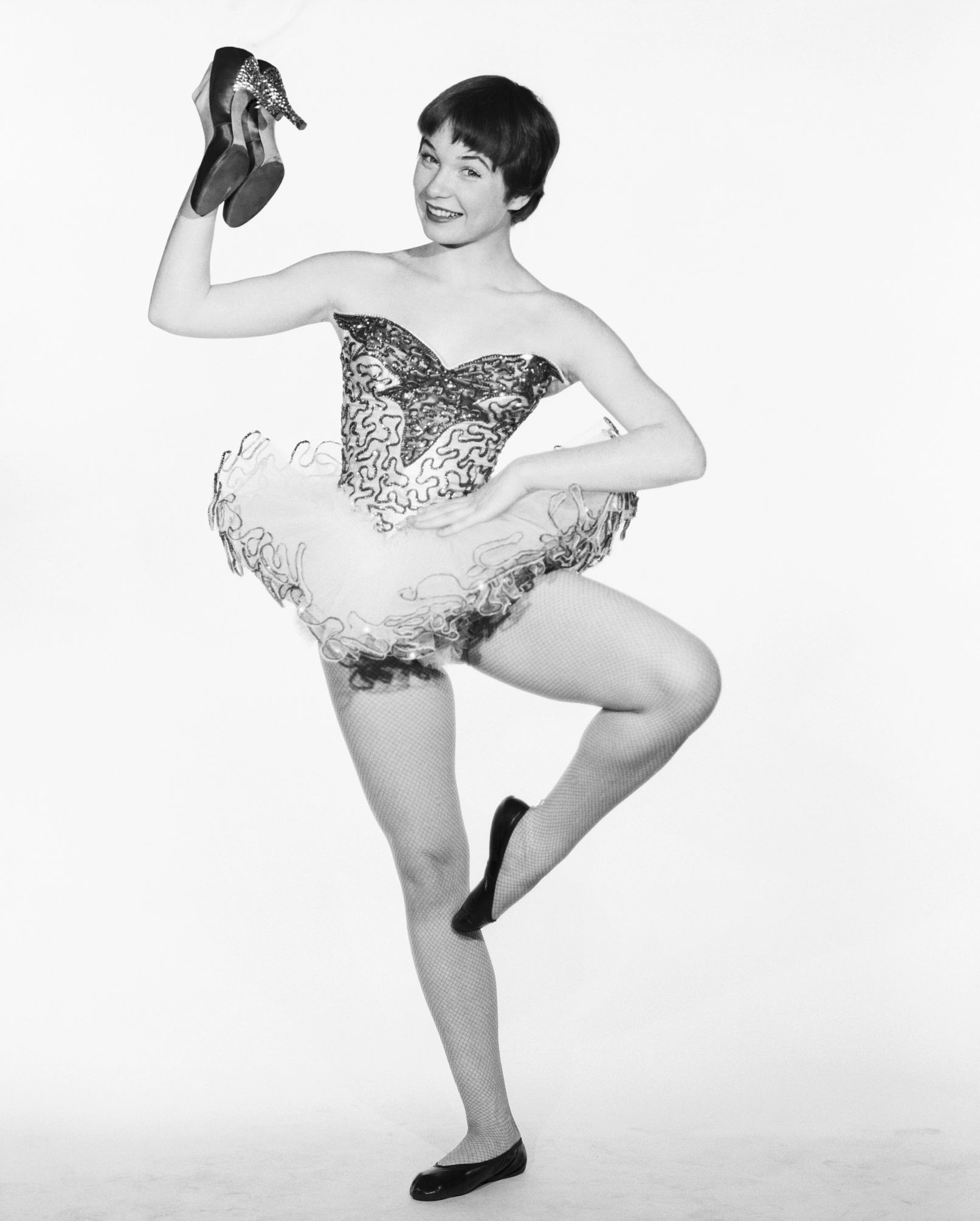 Shirley MacLaine holding her shoes while in a ballet costume