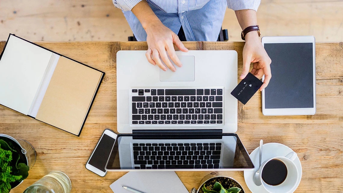 woman sitting at table with laptop tablet smartphone and credit card in hand