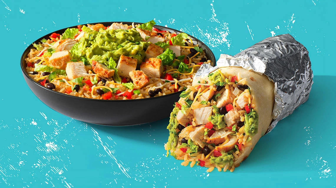 Moe's Southwest Grill chicken burrito wrapped in tortilla and foil with lettuce, guacamole, black beans, cheddar cheese, tomato and a chicken burrito bowl next to it