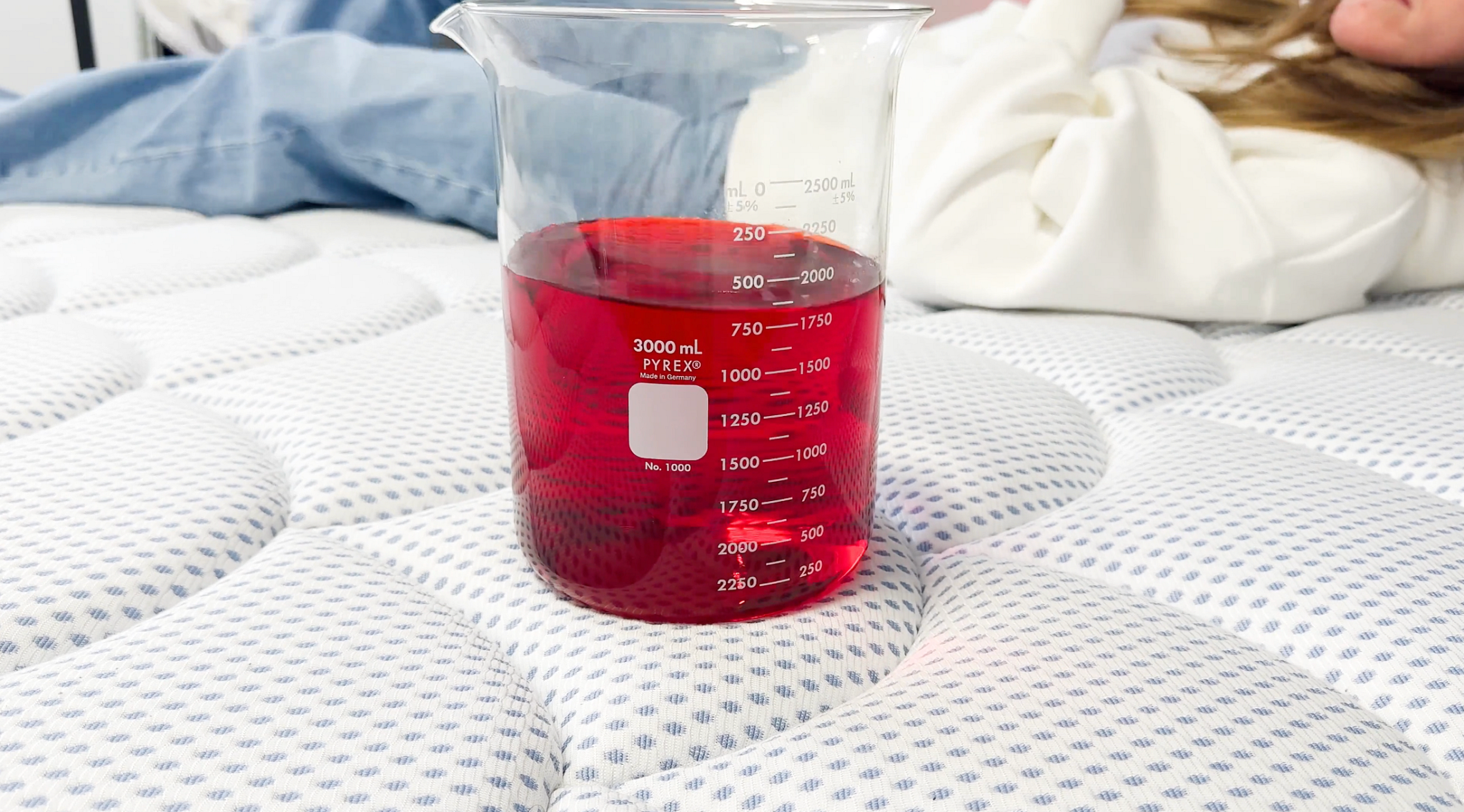 A beaker of red liquid sits on the surface of the DreamCloud Premier Hybrid mattress as a lab tester tests the bed’s motion isolation.