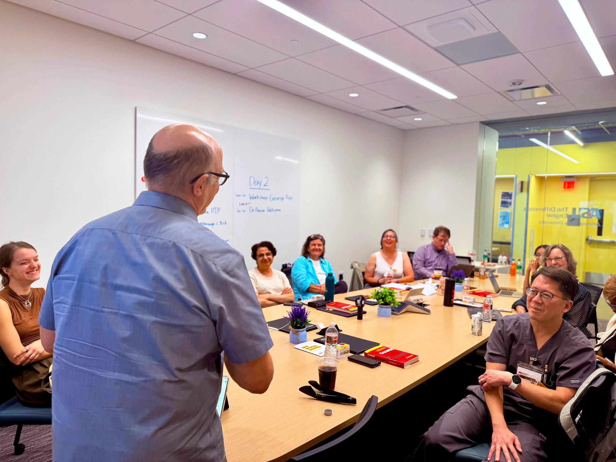 a group of people sitting at a board room table while a man stands and faces them