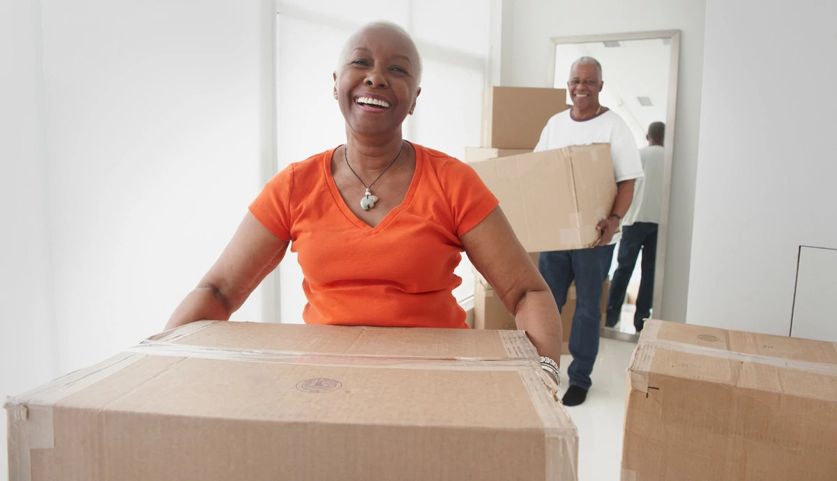 A mature African American woman carrying moving boxes into a new home. 