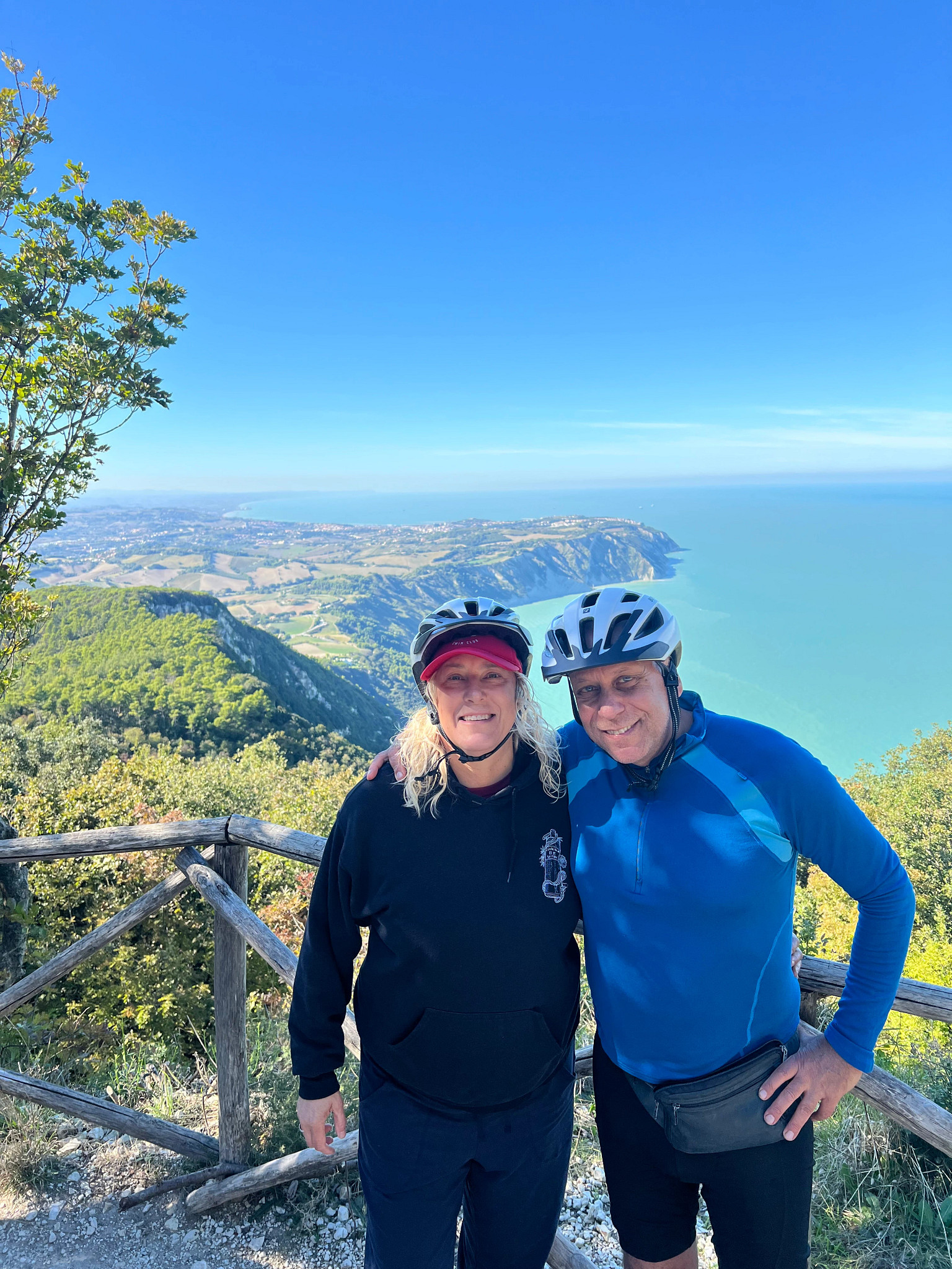 a woman and man posing for a picture while wearing biking gear on an overlook