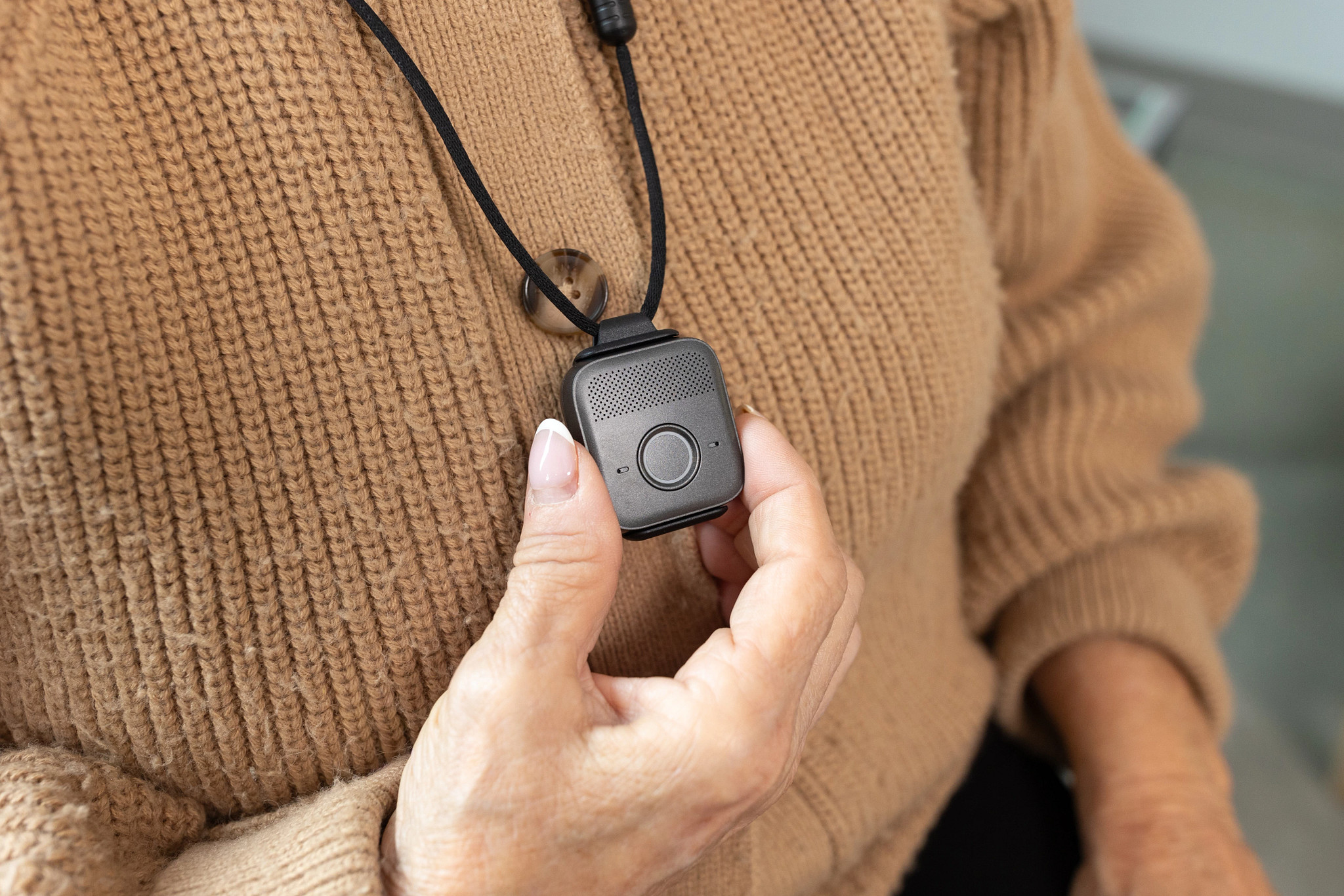 A woman holds the Bay Alarm Medical SOS Micro device while wearing the pendant around her neck.