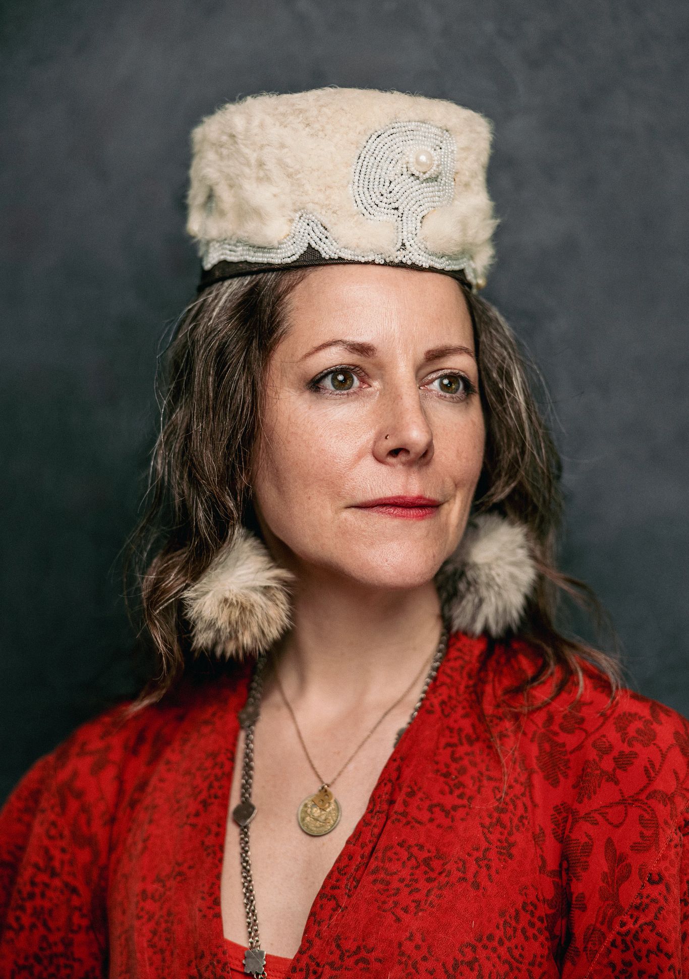 Best AARP Photos of 2024 a woman in a red dress with furry hat and earrings