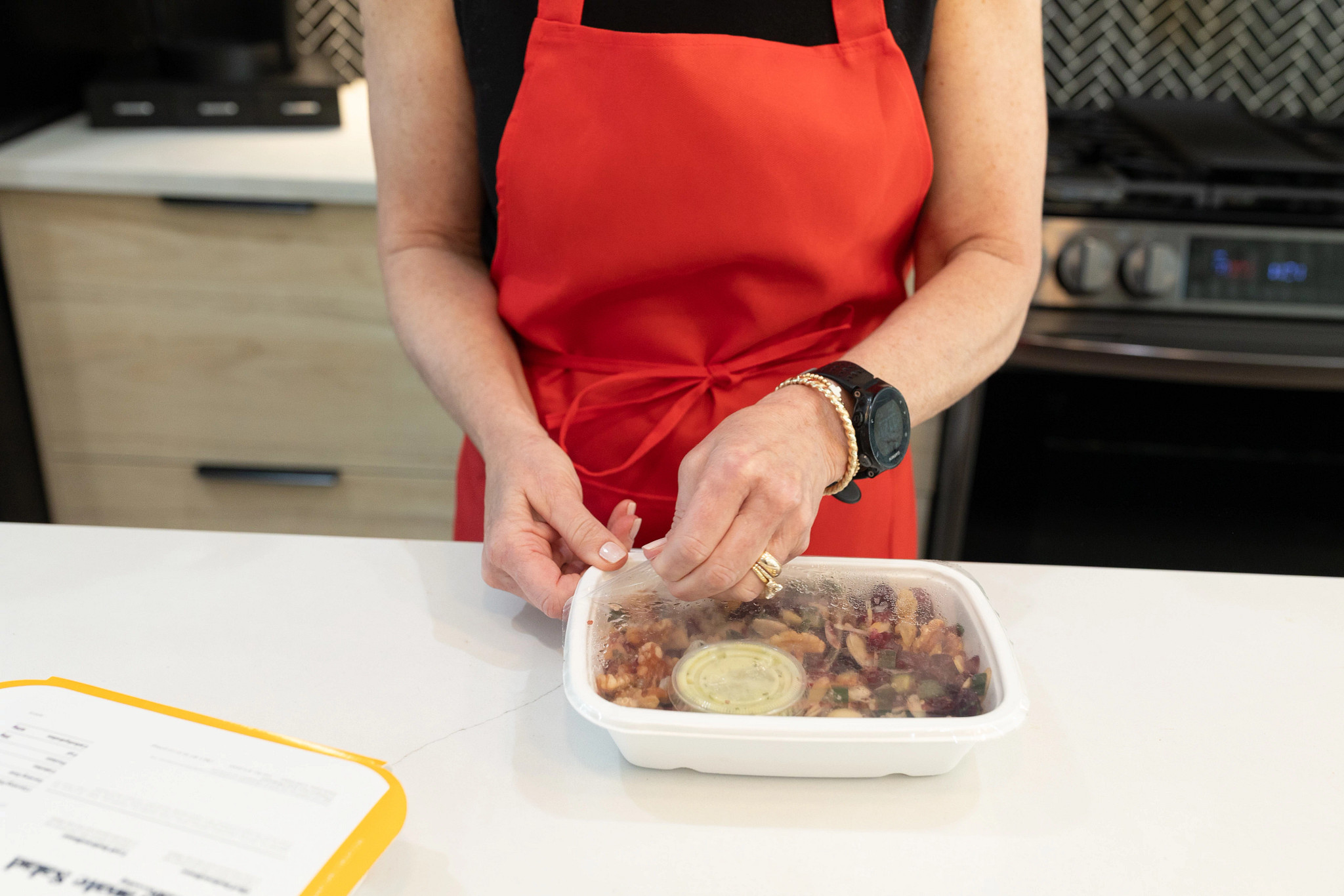 An older adult woman opening a CookUnity quinoa and pomegranate salad.