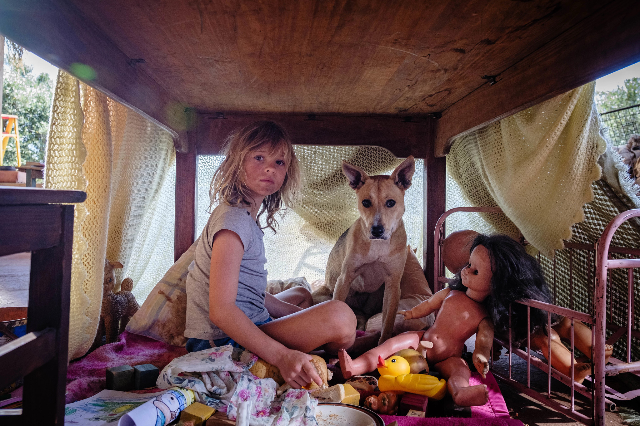 A young girl, a dog and a doll all under a partially covered table in a scene from the film Don't Let's Go to the Dogs Tonight